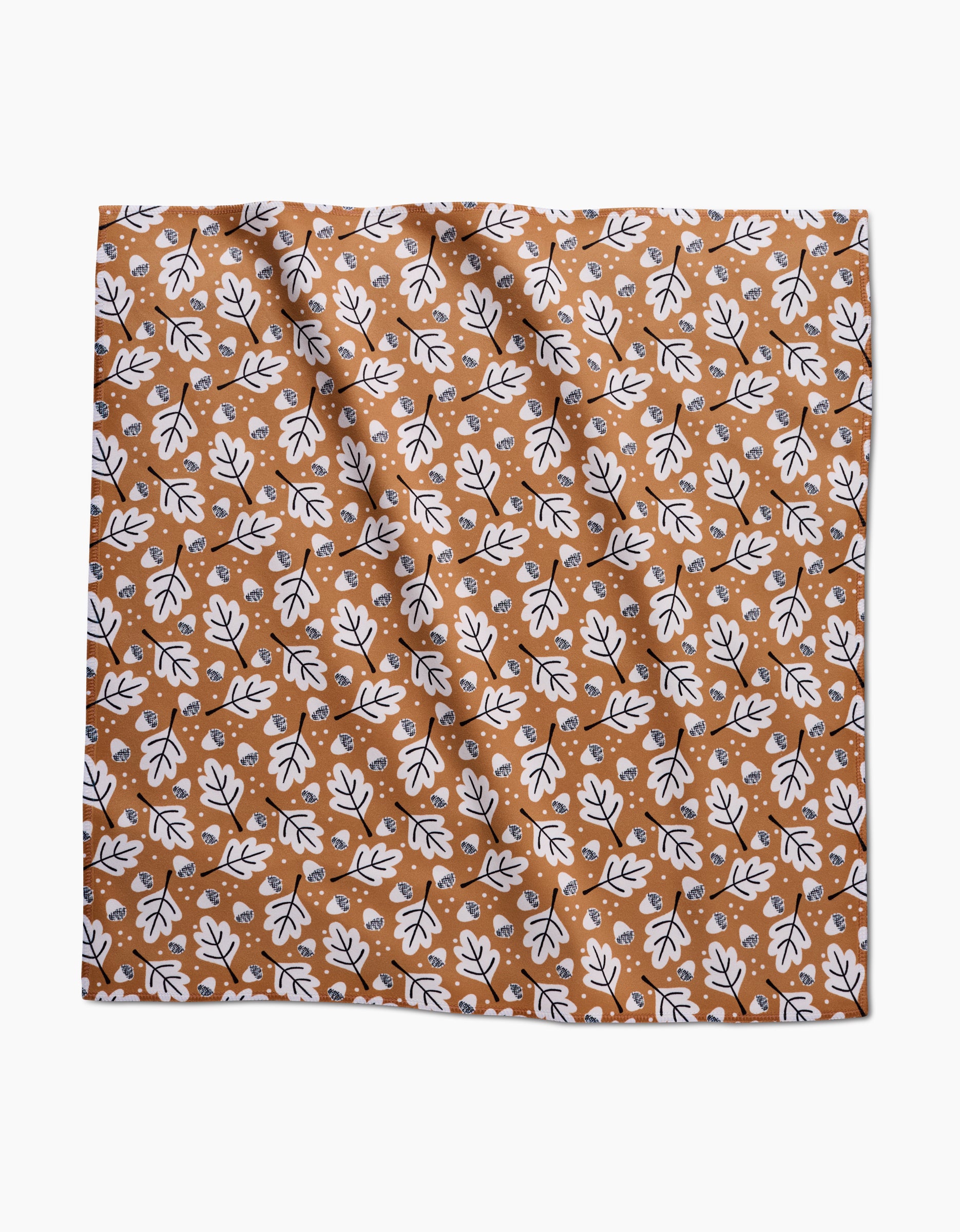 The Falling Acorns Dinner Napkin Set by Charlie Rowan Designs features a square, eco-friendly cloth with a white and black oak leaf pattern on brown, accented by scattered white dots and a slightly wrinkled texture.