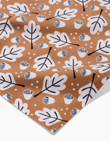 A close-up of Charlie Rowan Designs’ Falling Acorns fabric shows white oak leaves, crosshatched acorns, and small dots on brown—ideal for eco-friendly table linens or recycled napkins.