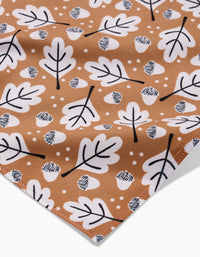 A close-up of Charlie Rowan Designs’ Falling Acorns fabric shows white oak leaves, crosshatched acorns, and small dots on brown—ideal for eco-friendly table linens or recycled napkins.