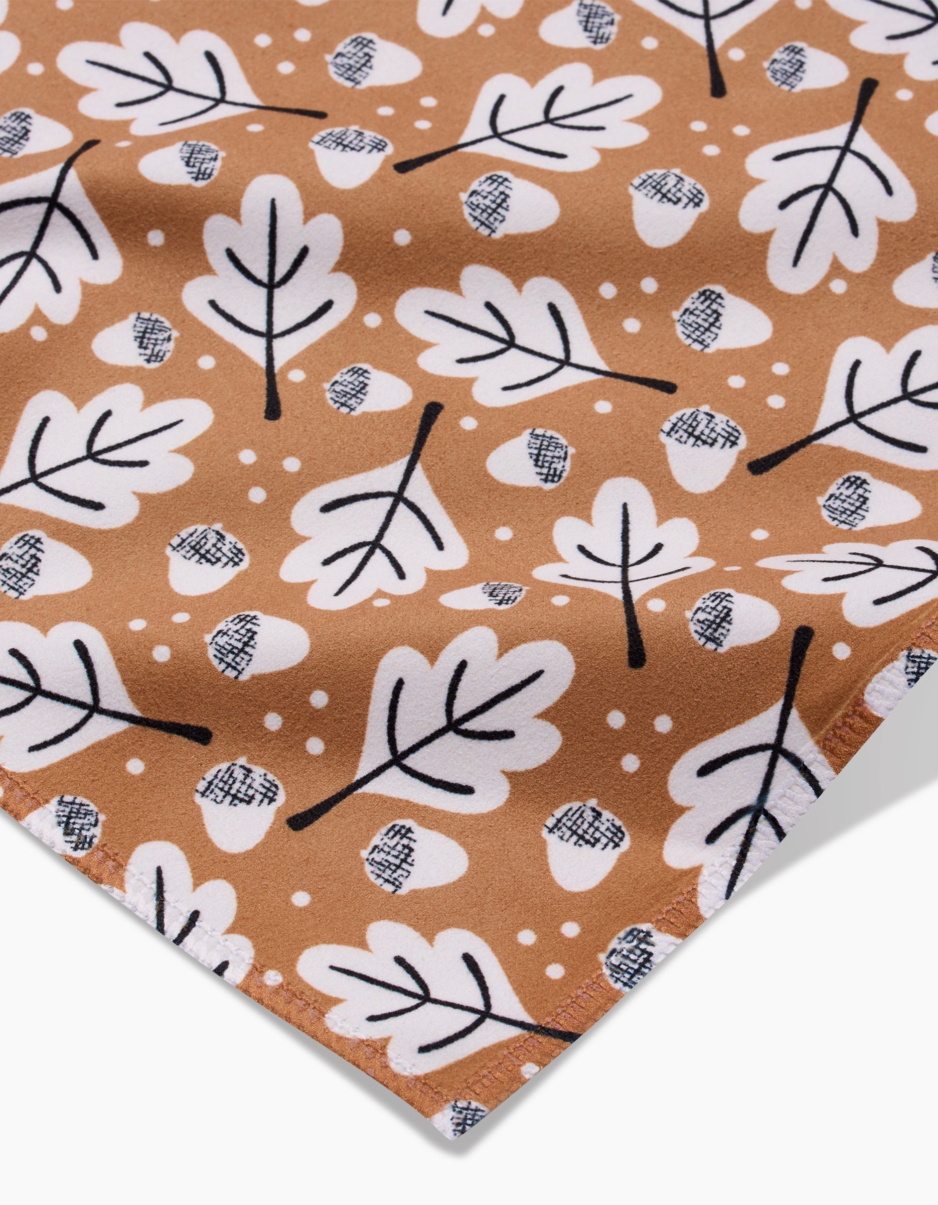 A close-up of Charlie Rowan Designs’ Falling Acorns fabric shows white oak leaves, crosshatched acorns, and small dots on brown—ideal for eco-friendly table linens or recycled napkins.