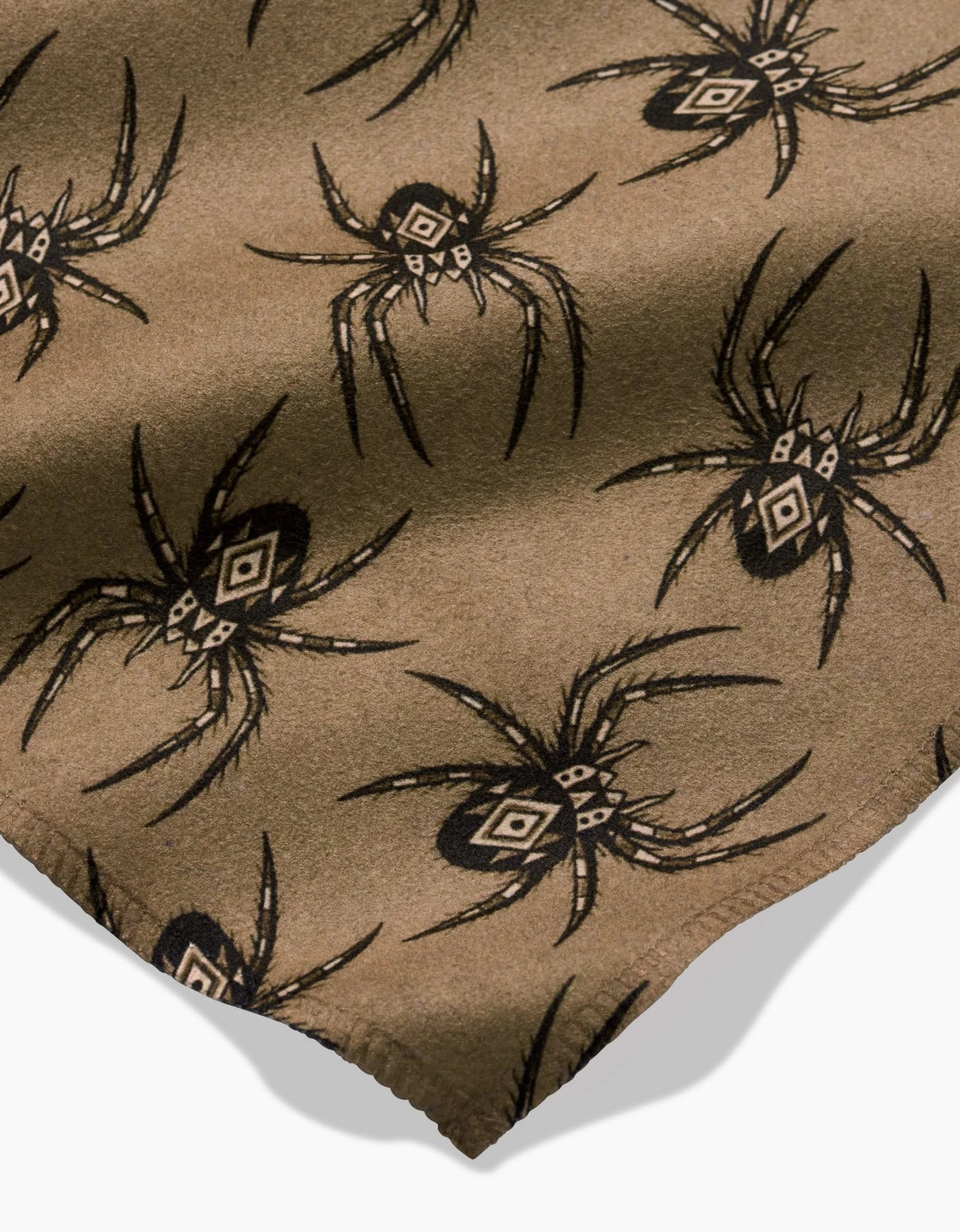 Flash by Cole Strem: A brown Geosuede fabric made from recycled materials, featuring a repeating black spider pattern with geometric details, displayed flat with a scalloped bottom edge.