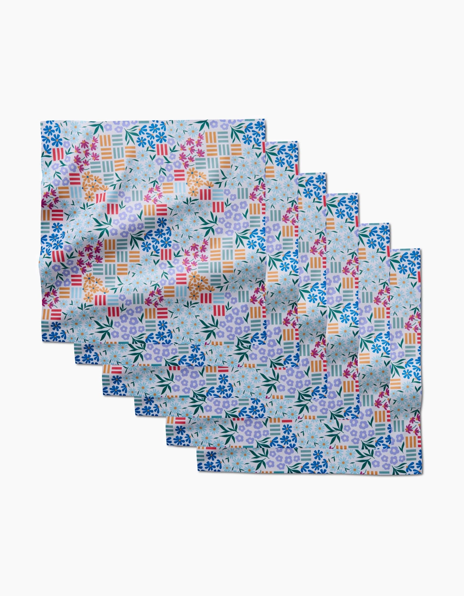 Eight folded Floral Garden Dinner Napkins by Charlie Rowan Designs are arranged in a fan. Made from recycled Geosuede, they display colorful geometric patchwork with floral, leaf, and stripe motifs in blue, pink, red, yellow, and green.