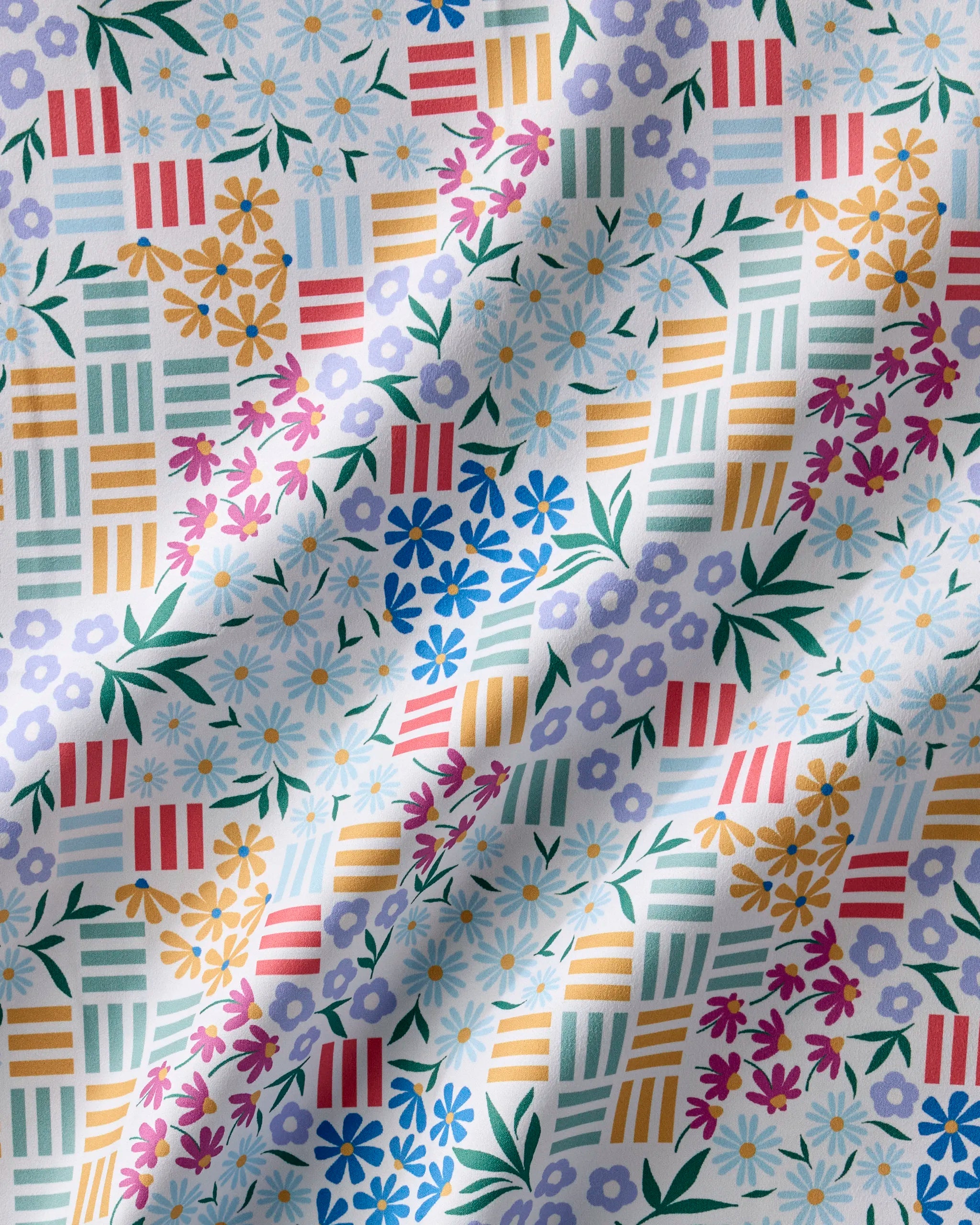 Floral Garden by Charlie Rowan Designs features vibrant daisies, blue and purple flowers, and geometric stripes. This eco-friendly, slightly wrinkled fabric is ideal for recycled dinner napkins or a whimsical napkin set.
