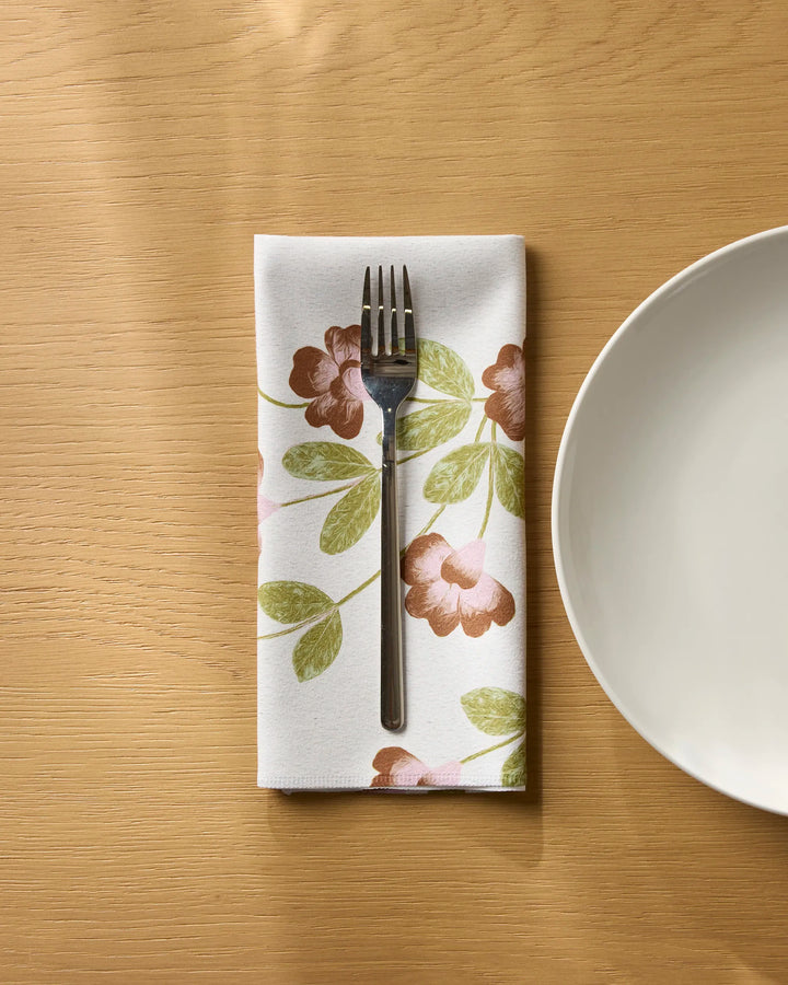 A fork rests on a folded Geometry Flower Tower eco-friendly napkin beside a white plate on a light wooden table.