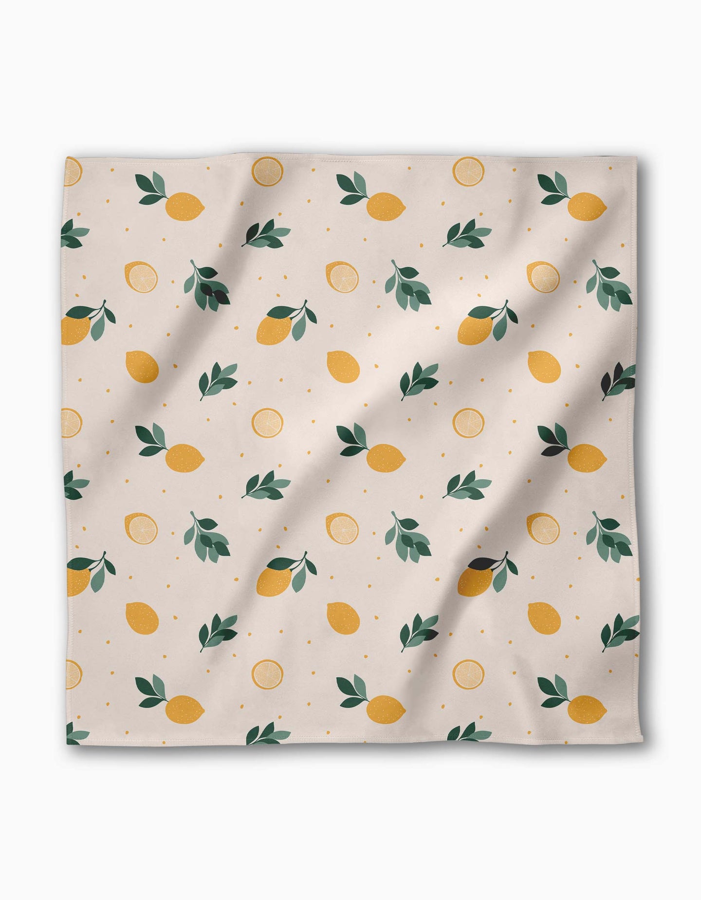 The Freshly Picked dinner napkin by Sara Mari features yellow lemons, green leaves, and lemon slices on light beige Geosuede made from recycled materials. Slight wrinkles in the fabric add a relaxed touch.