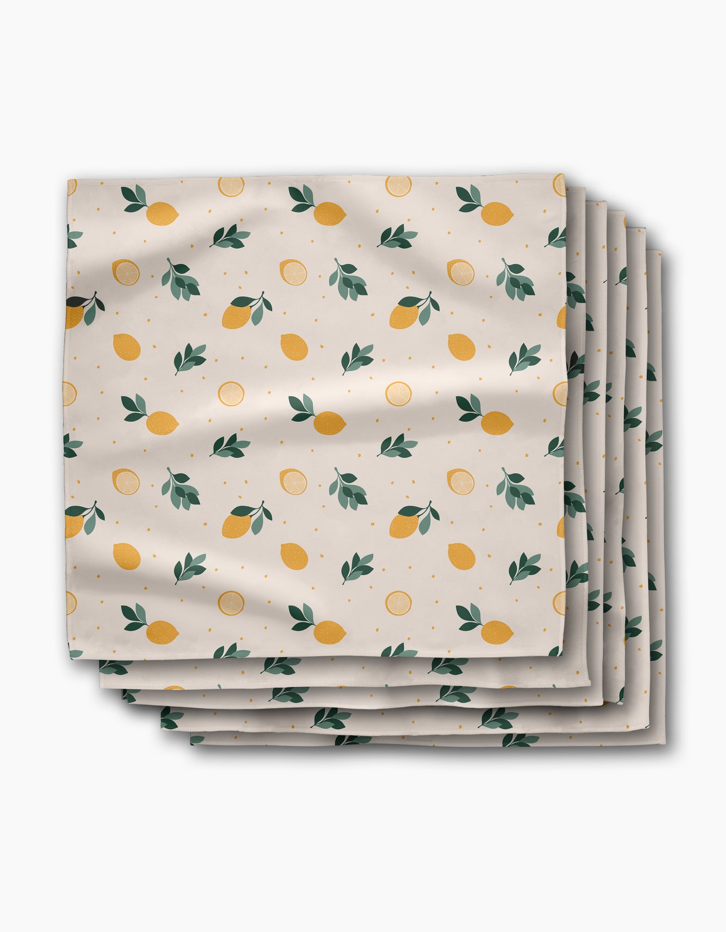 A stack of Sara Mari Freshly Picked Dinner Napkins in Geosuede fabric, featuring yellow lemons, green leaves, and orange dots on a white background.