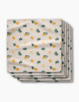 A stack of Sara Mari Freshly Picked Dinner Napkins in Geosuede fabric, featuring yellow lemons, green leaves, and orange dots on a white background.