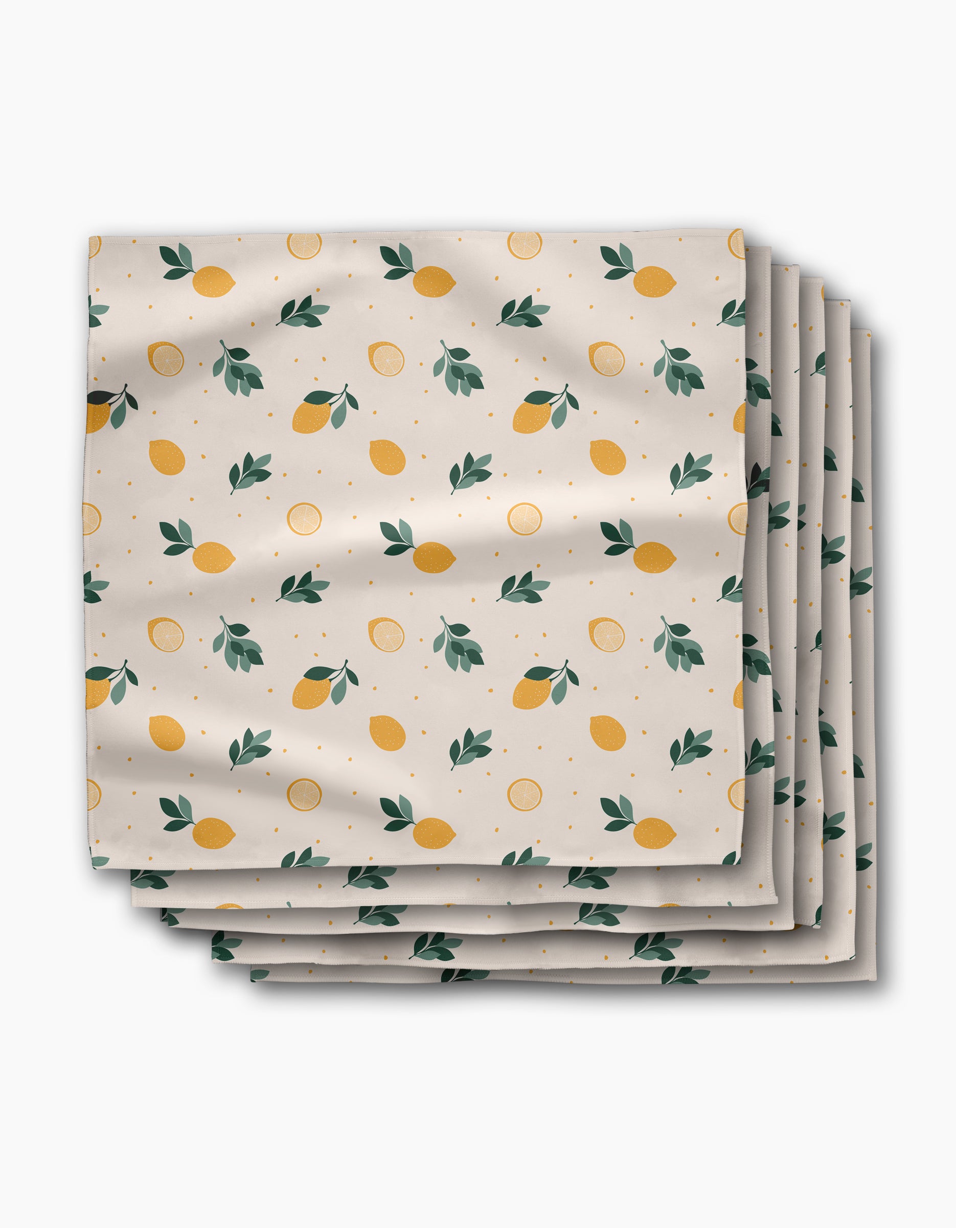 A stack of Sara Mari Freshly Picked Dinner Napkins in Geosuede fabric, featuring yellow lemons, green leaves, and orange dots on a white background.
