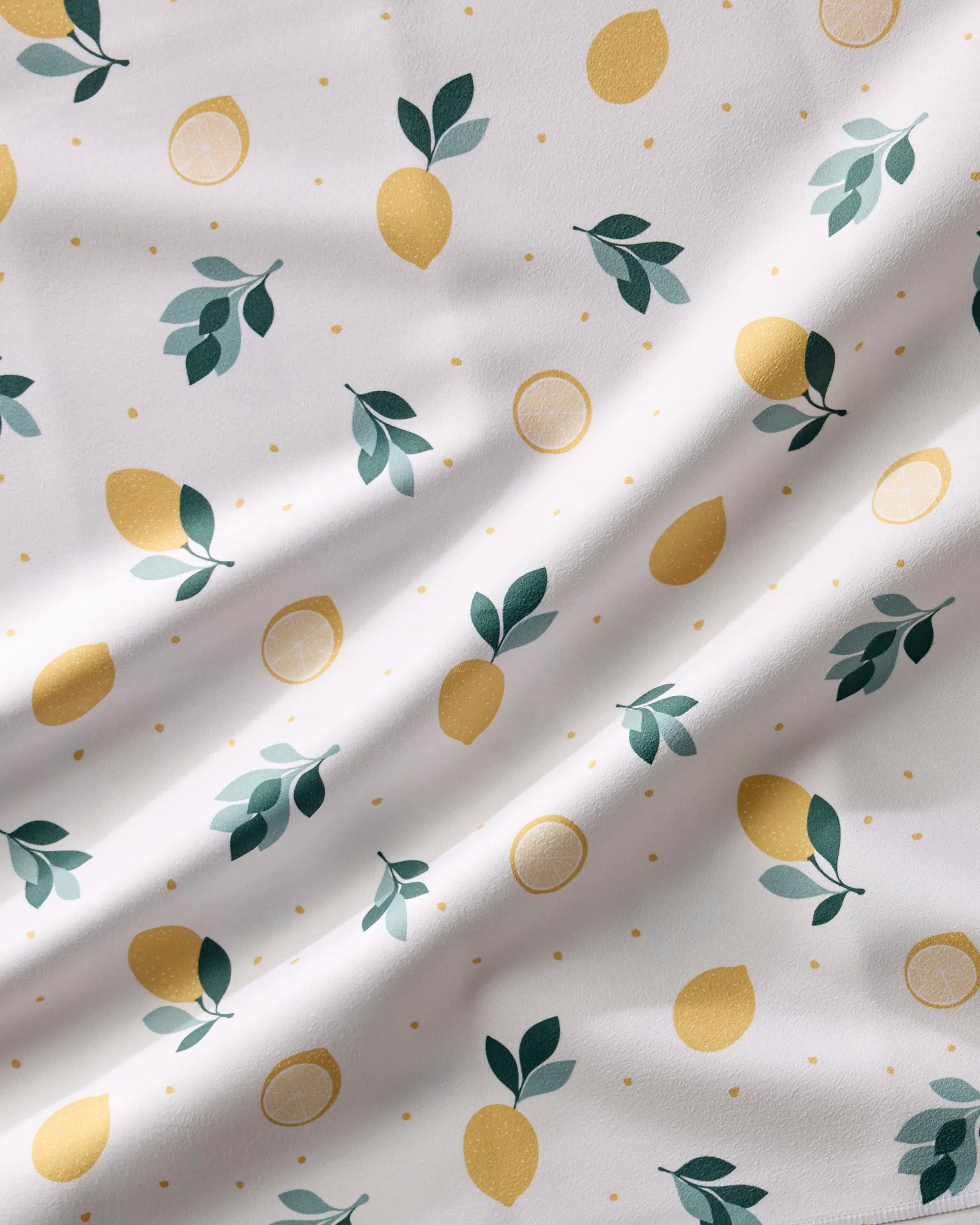 The "Freshly Picked" dinner napkins by Sara Mari feature a white fabric with yellow lemons, lemon slices, green leaves, and small yellow dots. Soft and absorbent with a slightly wrinkled look, they add fresh charm to any summer table.