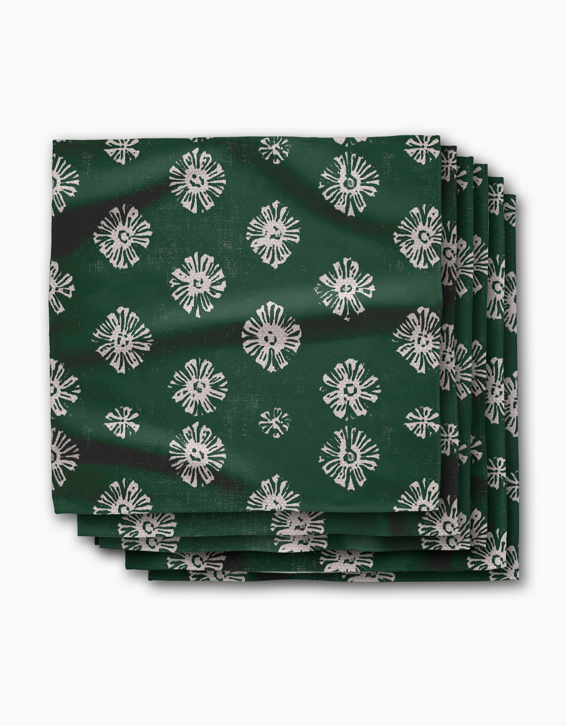 Four green Freya dinner napkins by Geometry, made from soft Geosuede fabric with white geometric floral patterns, are stacked against a plain white background.