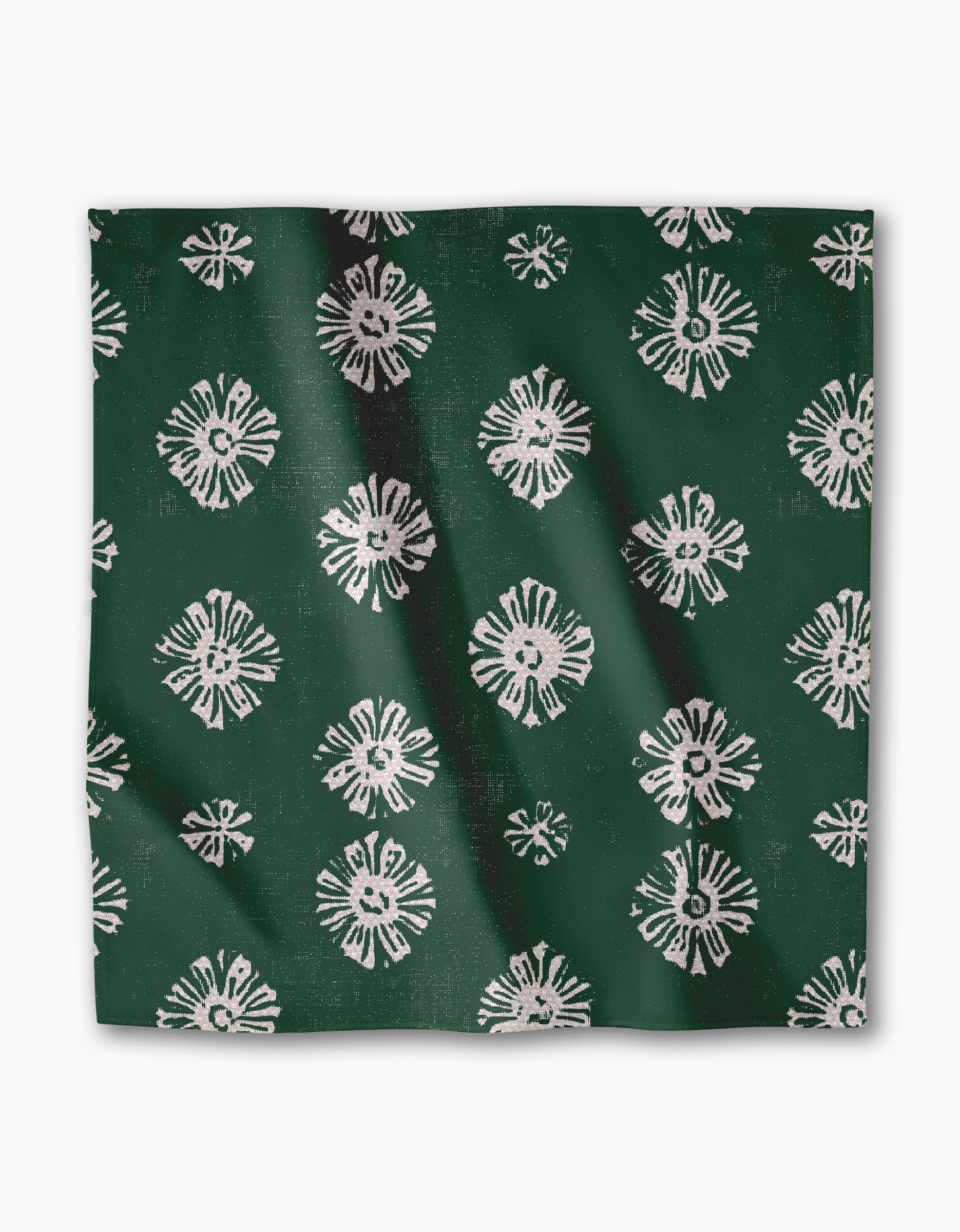 The Freya dinner napkin by Geometry features dark green Geosuede fabric with an abstract white floral pattern. Made from recycled materials, it has a soft feel, slight creases, and an evenly textured surface.