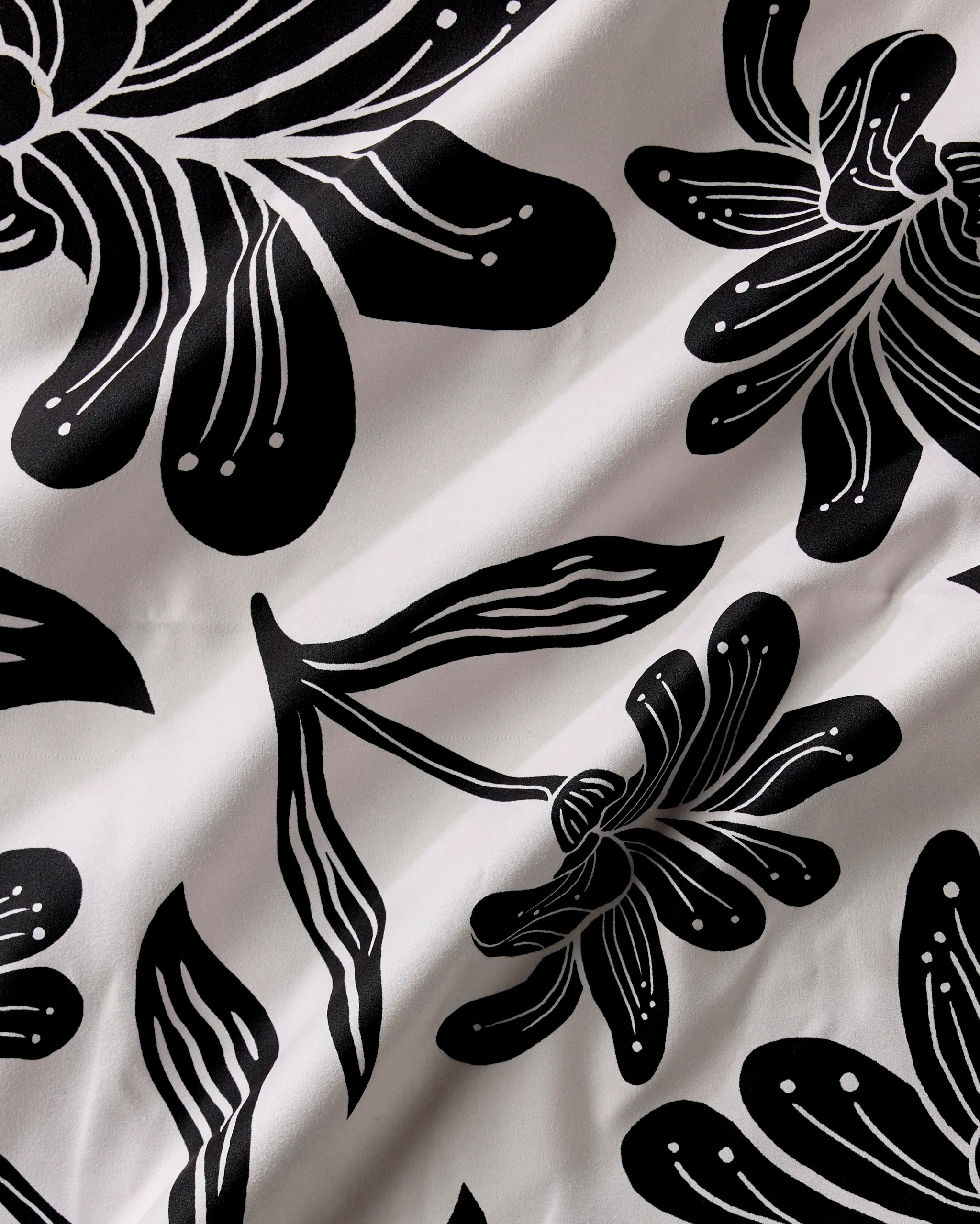 Giant Lush Floral by Geometry features black and white fabric with a bold abstract floral design, outlined flowers and leaves, white lines and dots, and a slightly wrinkled texture—ideal for eco-friendly napkins.