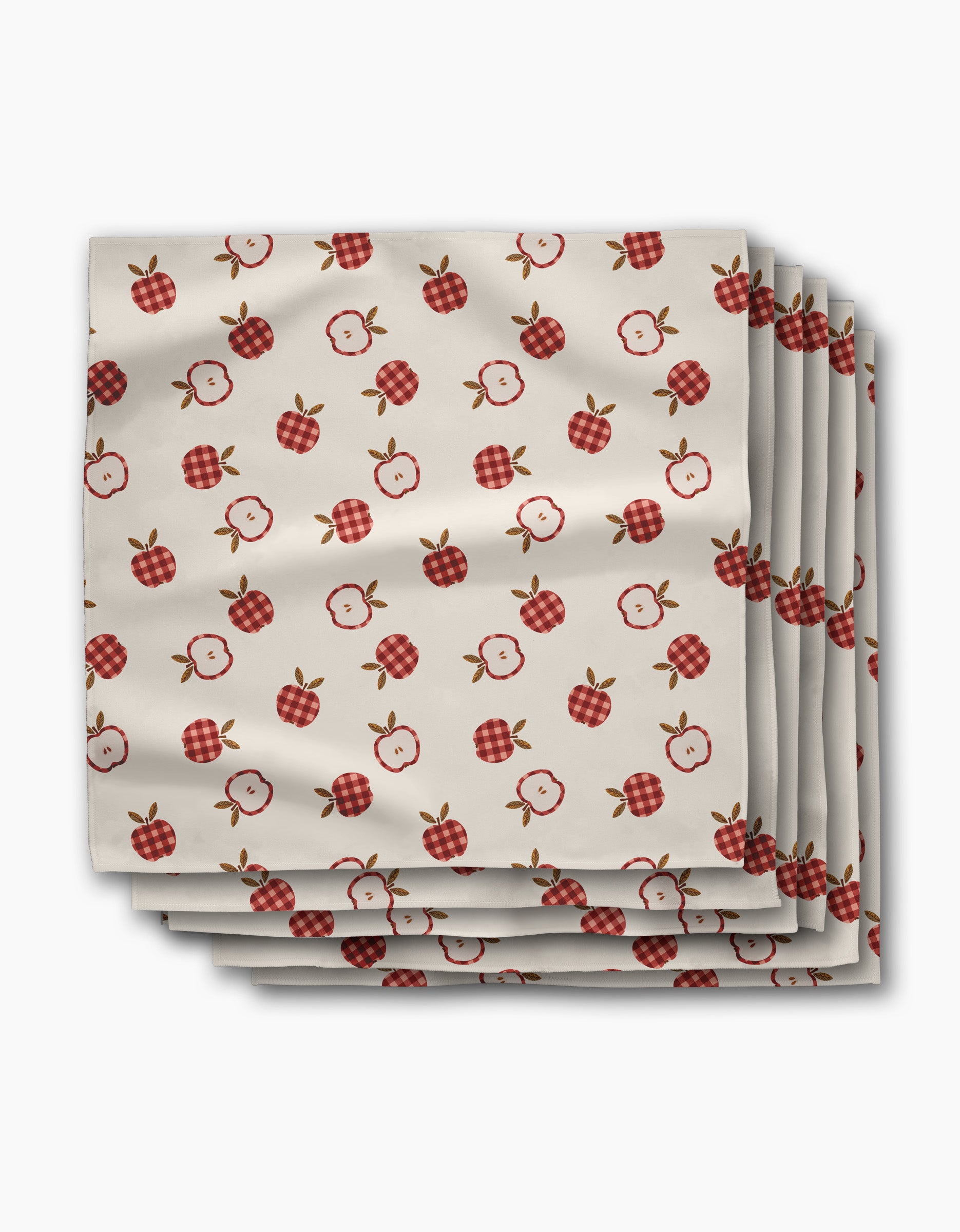 A stack of Gingham Apples dinner napkins by Teri the Butter, made from white recycled Geosuede fabric, displays a repeating pattern of solid, checkered, and sliced red apples on a crisp white background.