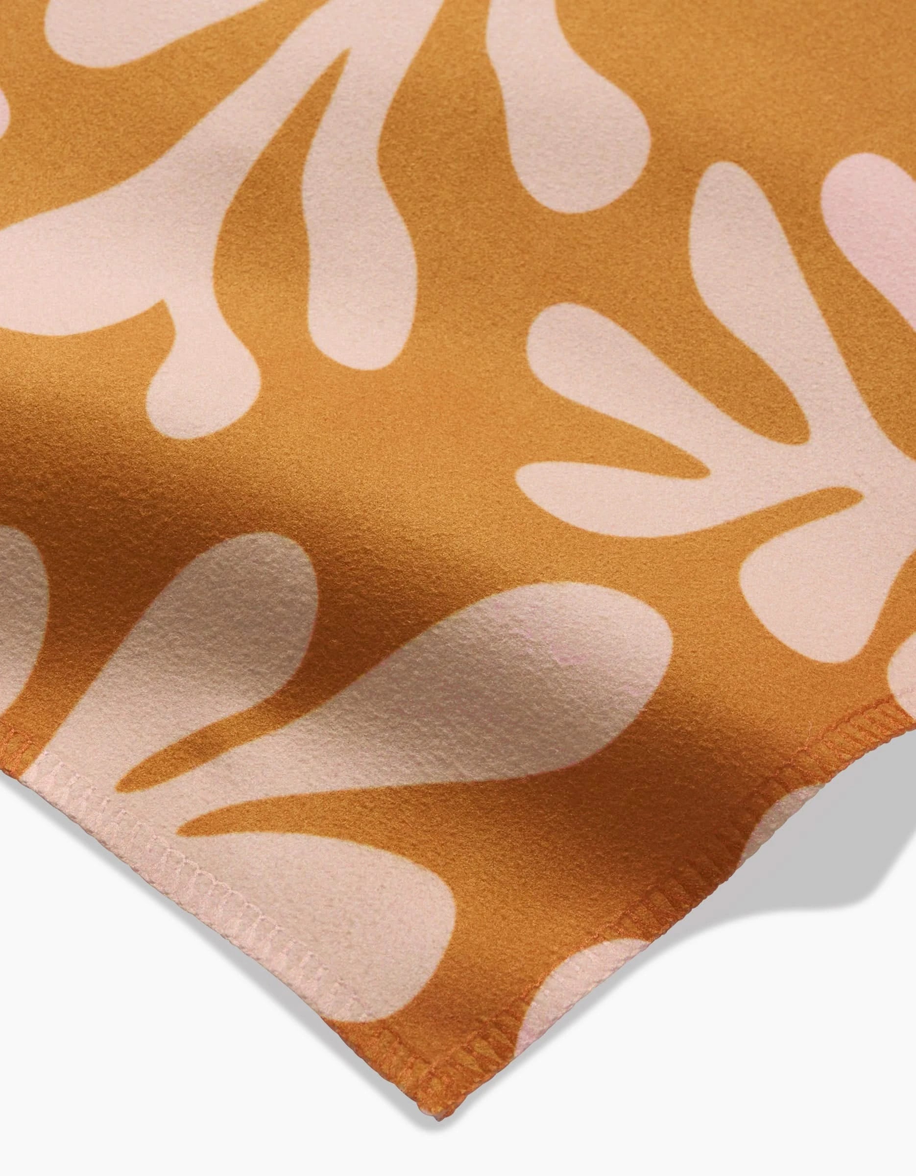 A close-up of GEOMETRY’s Golden Fall Geosuede shows its unique texture, made from recycled materials, with a mustard yellow background and light pink abstract shapes like leaves or petals. The fabric edge appears at the bottom right.
