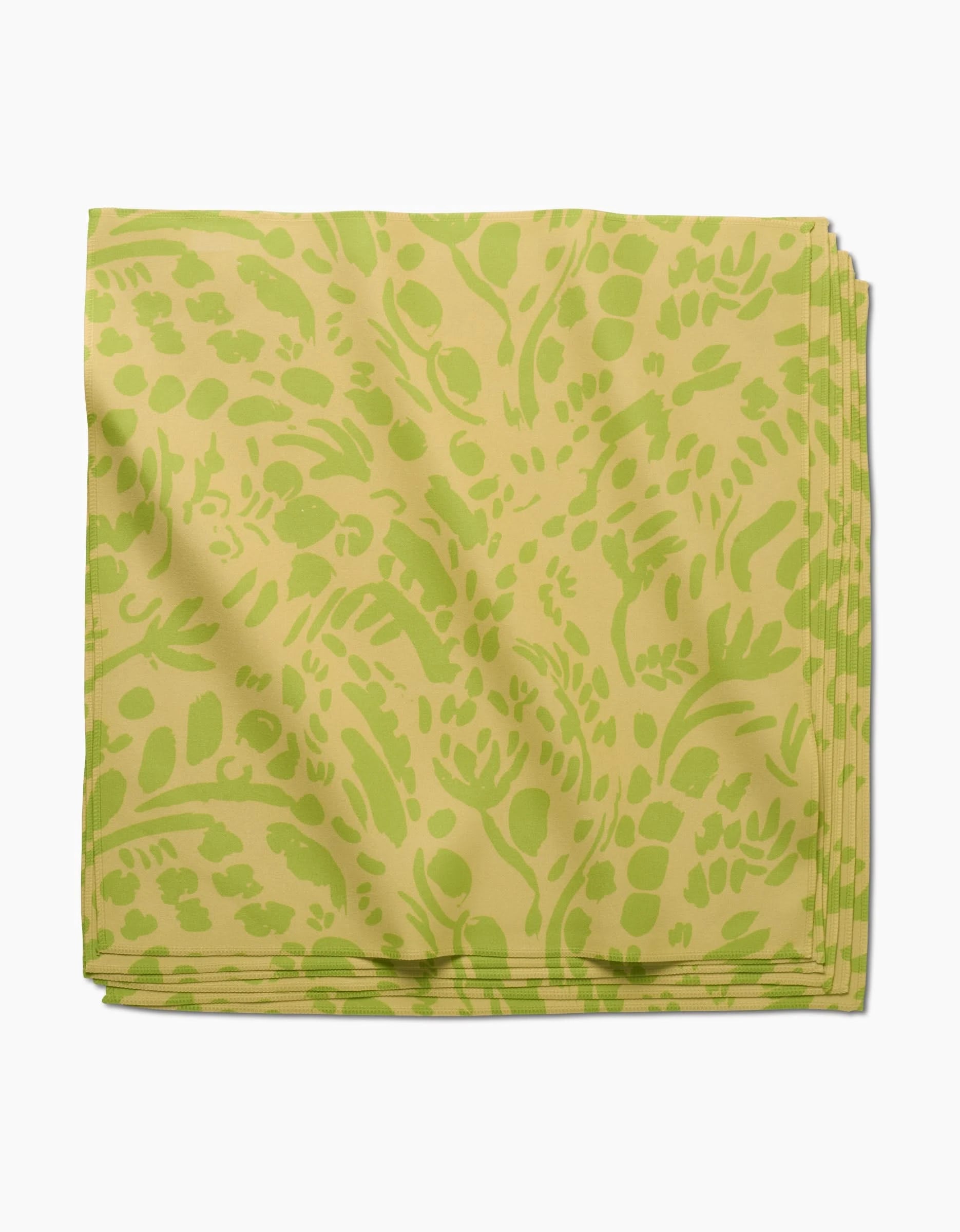 The Green Spring dinner napkin by Sareka Unique features light yellow Geosuede fabric with a green abstract botanical pattern, folded neatly and displayed against a white background.