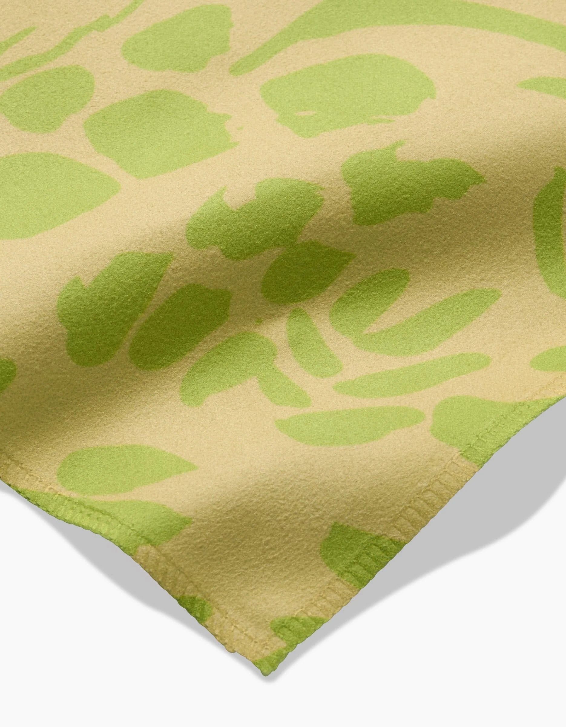 A close-up of Sareka Unique’s Green Spring in beige Geosuede, showcasing an irregular green abstract pattern and visible edge stitching. Crafted from recycled materials, it casts a soft shadow on a white surface.