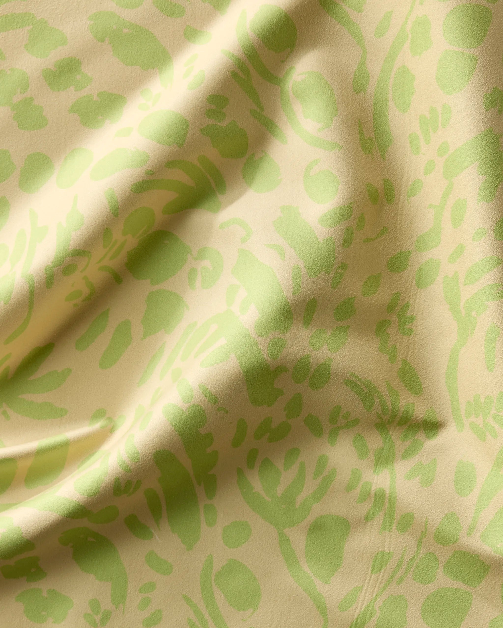 A close-up of the Sareka Unique Green Spring dinner napkin set, featuring light yellow Geosuede fabric with an abstract green floral and leaf pattern, highlighting its gentle folds and soft texture.