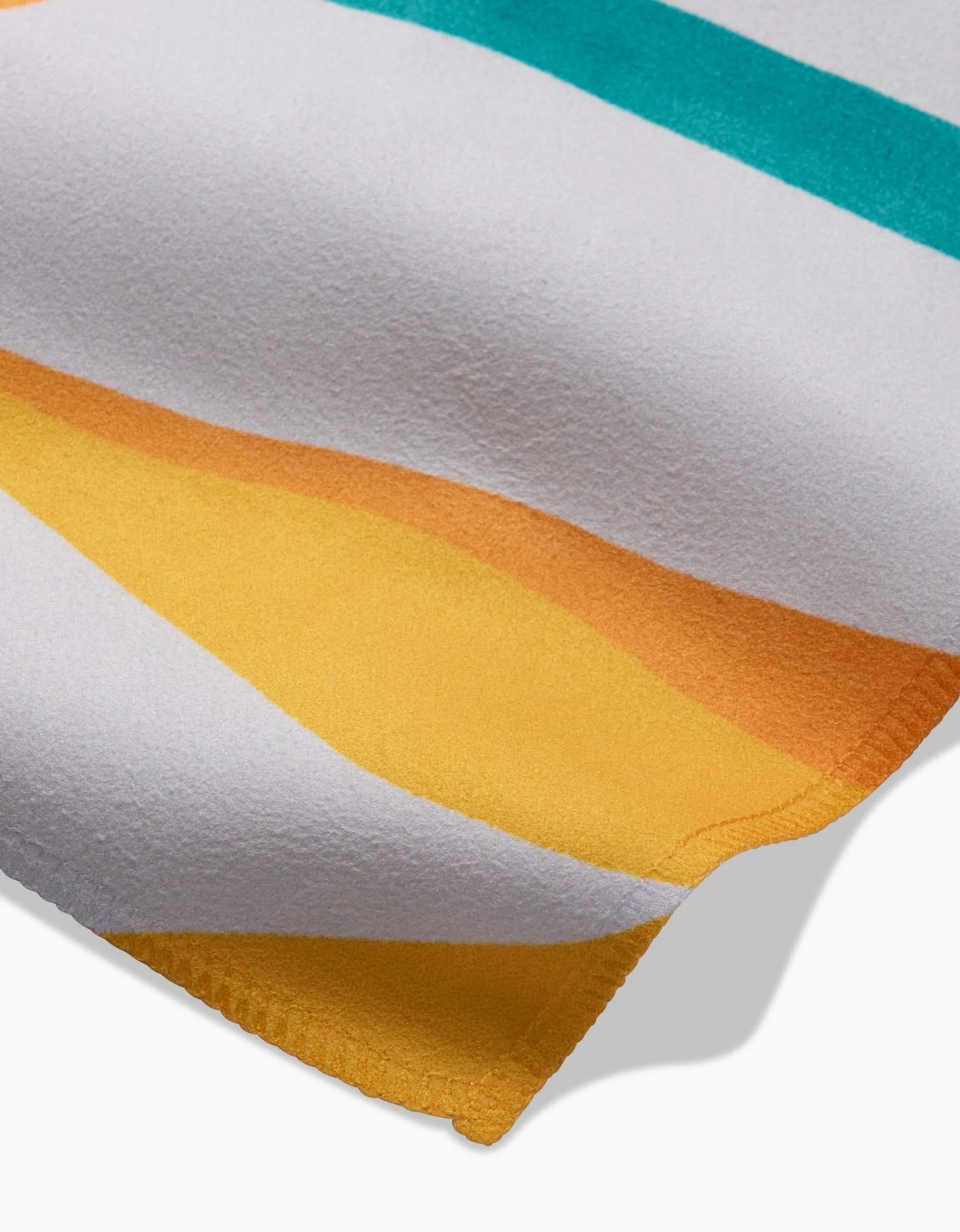 A close-up of the GEOMETRY Growth towel shows its textured surface and curved corner, with horizontal stripes in white, yellow, orange, and teal—evoking the absorbent feel of dinner napkins.