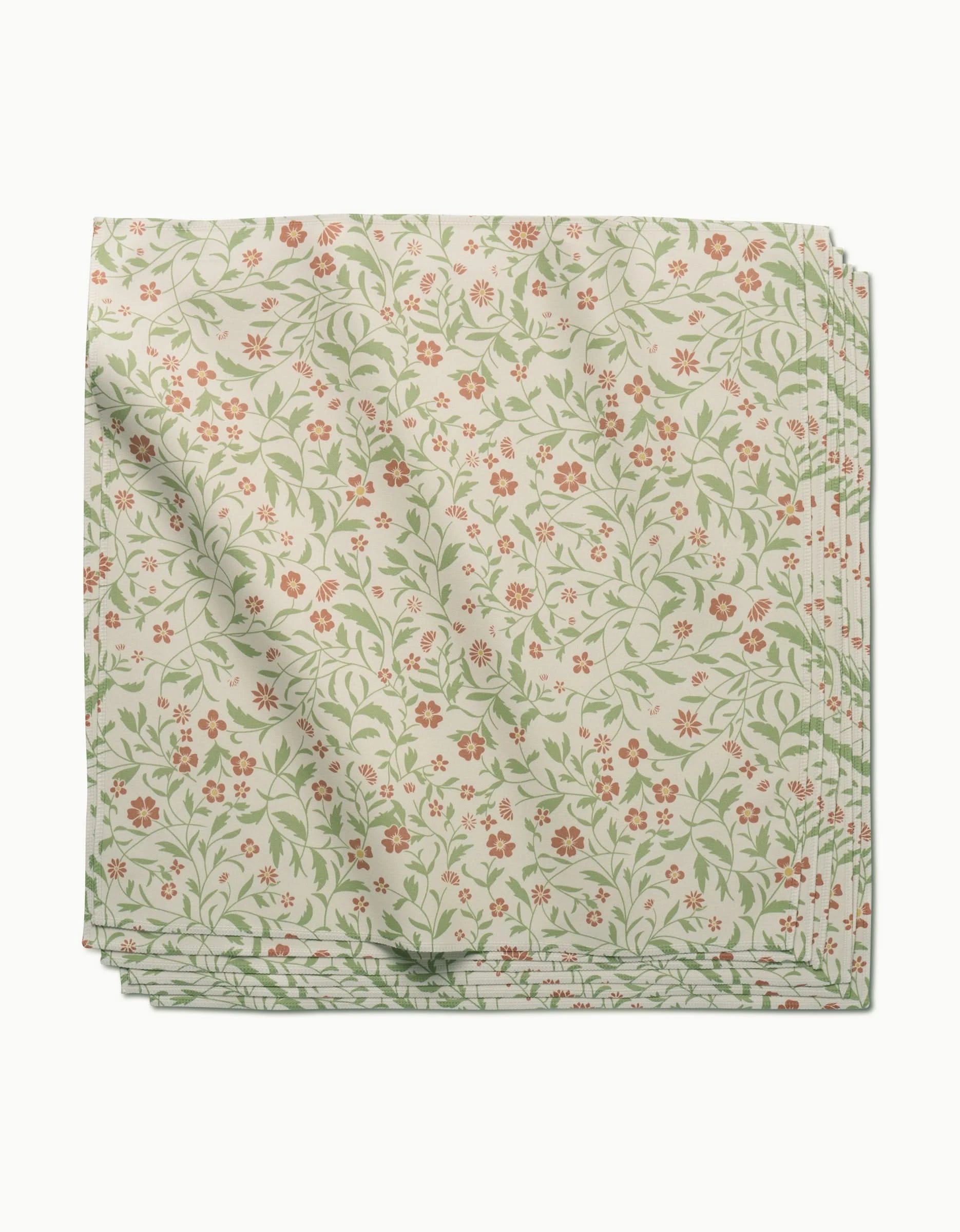 A neatly folded stack of cream-colored Danelys Sidron Hawthorns Geosuede dinner napkins, featuring a green vine and red floral pattern, displayed on a white background.