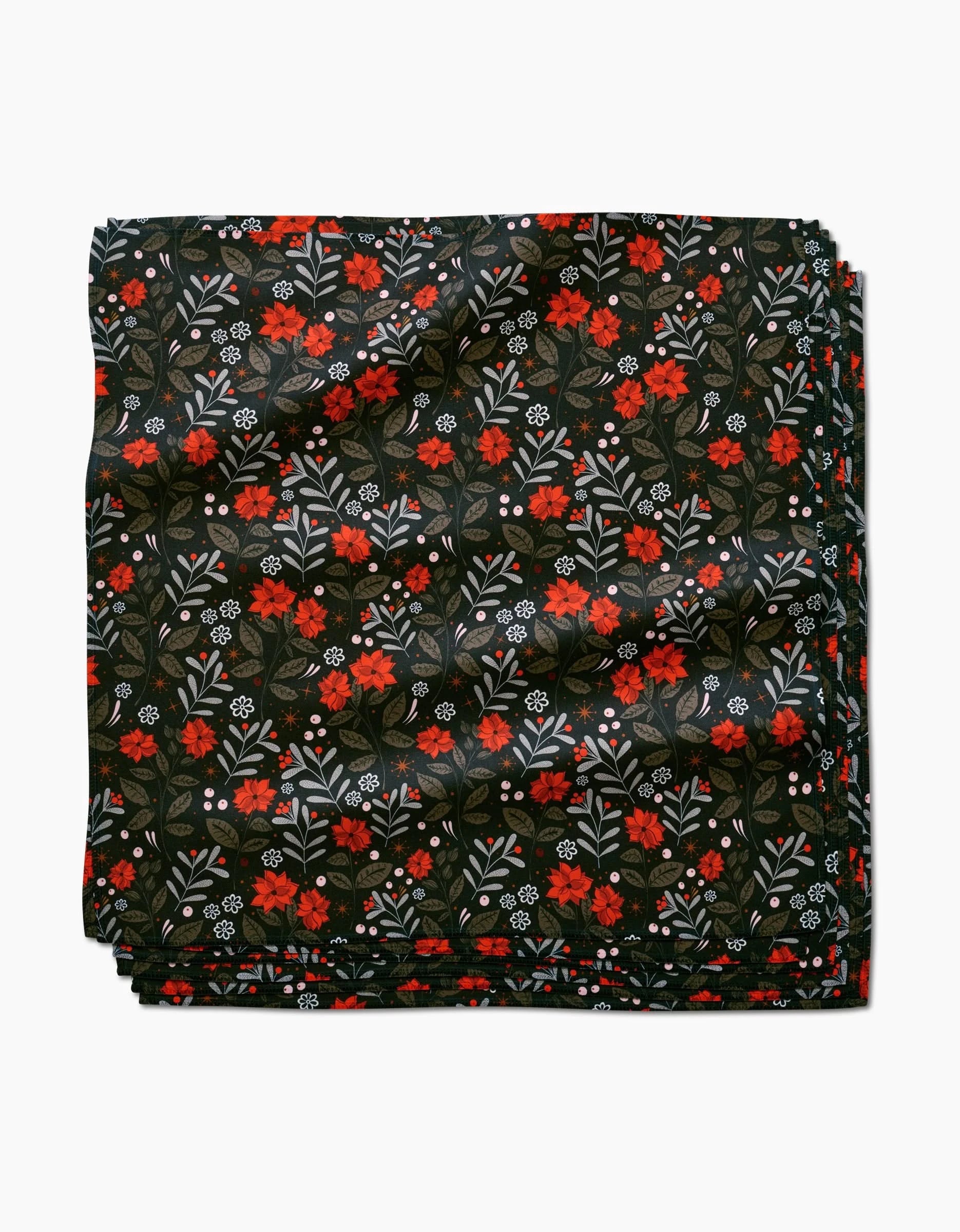 The Holiday Floral reusable napkin by Charlie Rowan Designs features a neatly folded design with a dark background and floral pattern of red flowers, green leaves, and small white accents.