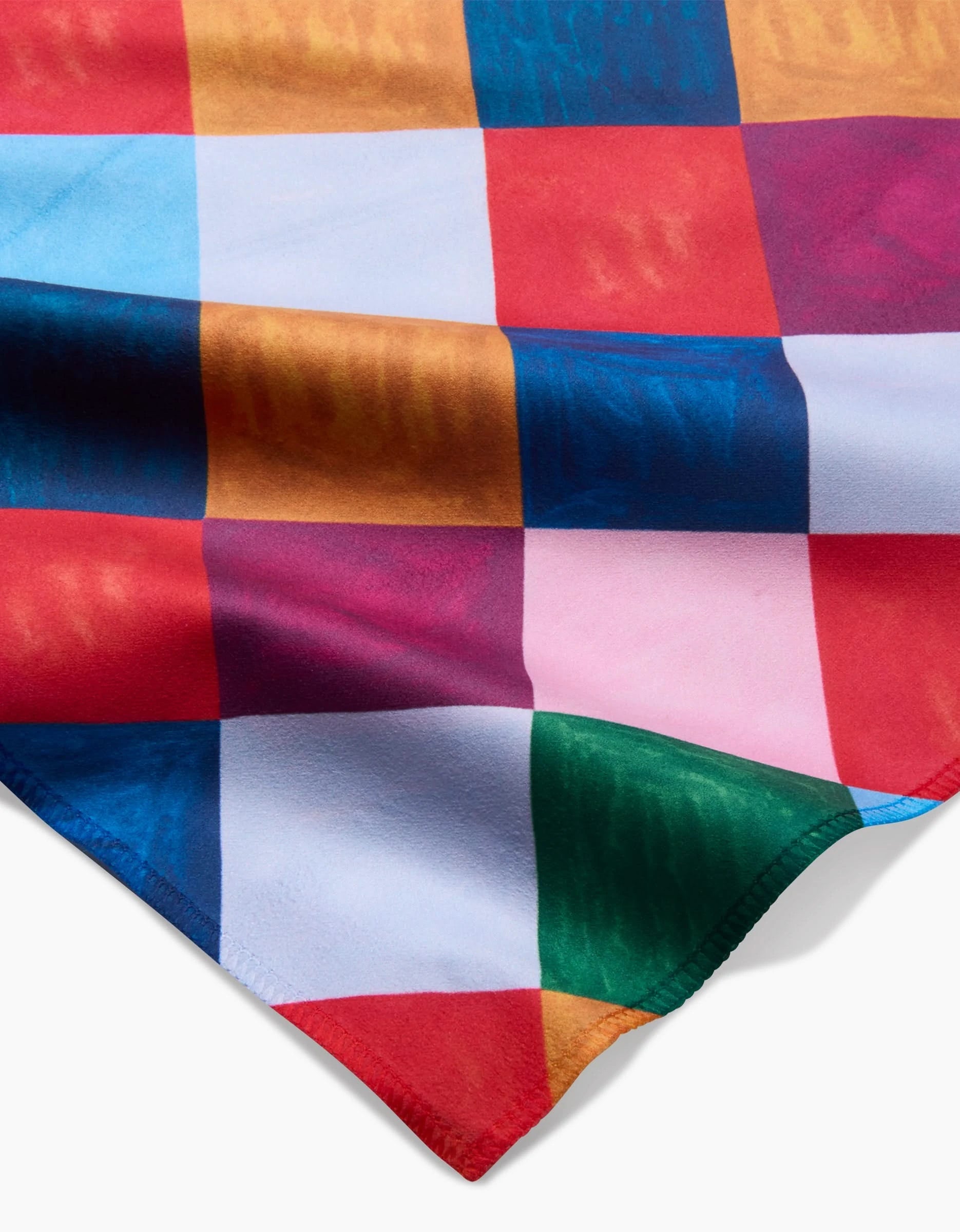 A close-up of Daria Solak’s Holiday Harlequin recycled dinner napkin set shows a multicolored checkered pattern with red, blue, green, pink, yellow, and white squares and a slightly folded corner.