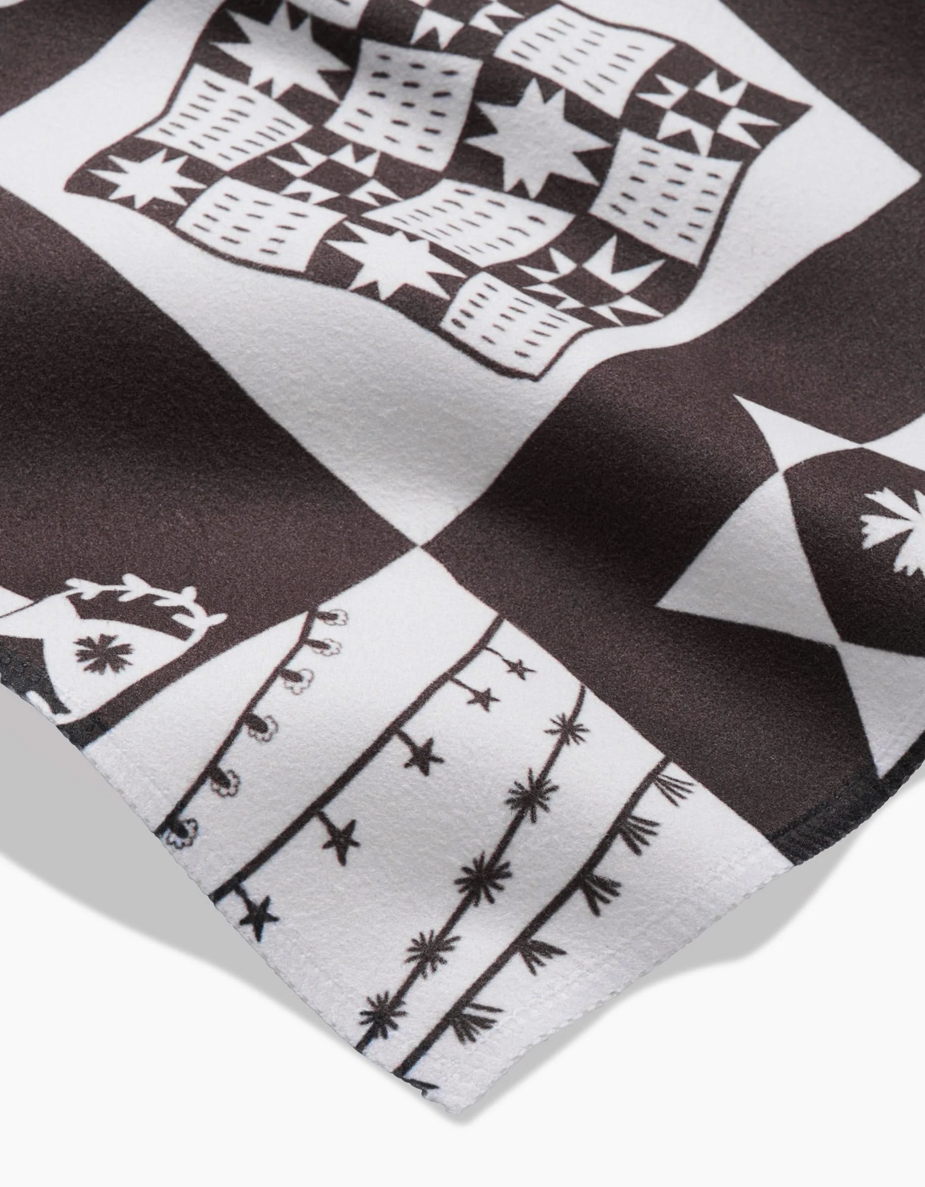A close-up of the Holiday Treats Dinner Napkin Set by Elana Gabrielle in black and white Geosuede, featuring bold geometric and star-like patterns with a decorative border of lines and shapes along the edge.