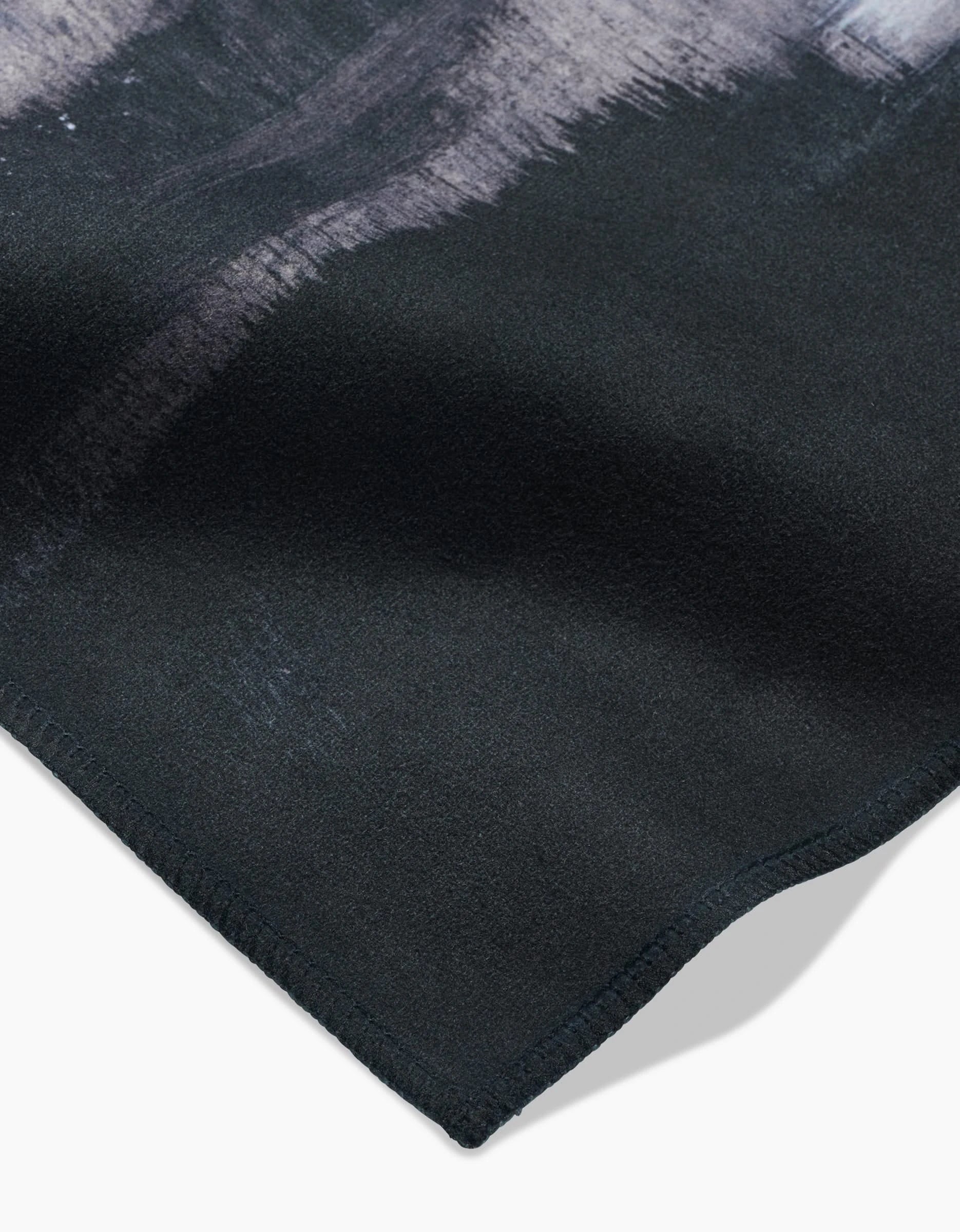 A close-up of Icelandic Elements by Jennifer Janesko shows black Geosuede with a soft texture, subtle light gray and white brushstroke patterns, and neatly stitched edges—ideal for elegant dinner napkins.