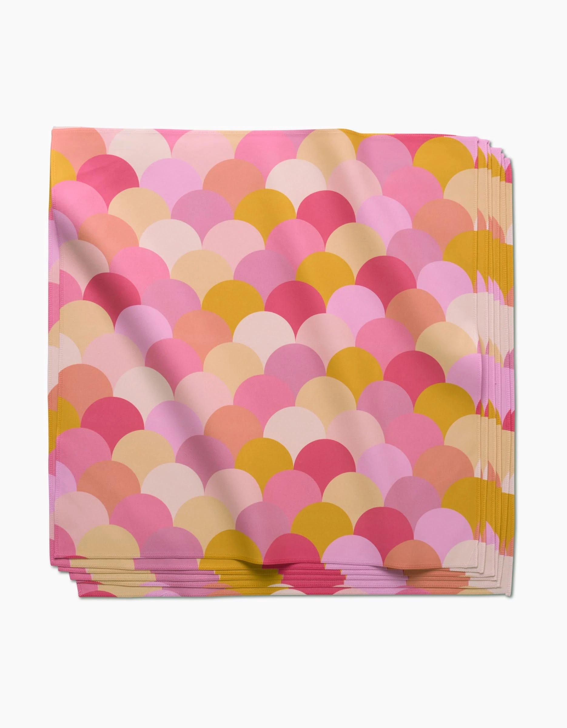 A stack of eco-friendly GEOMETRY Inherit Dinner Napkins made from Geosuede fabric, featuring a scalloped pattern in pink, yellow, and peach on white.