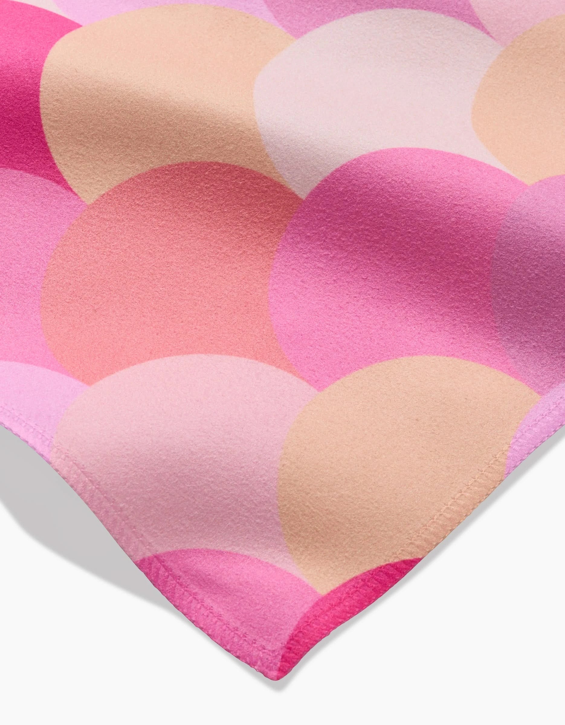 A close-up of an Inherit napkin by GEOMETRY highlights its pink and beige scalloped Geosuede fabric, featuring soft texture, finished edges, and eco-friendly appeal—perfect for stylish Dinner Napkins.