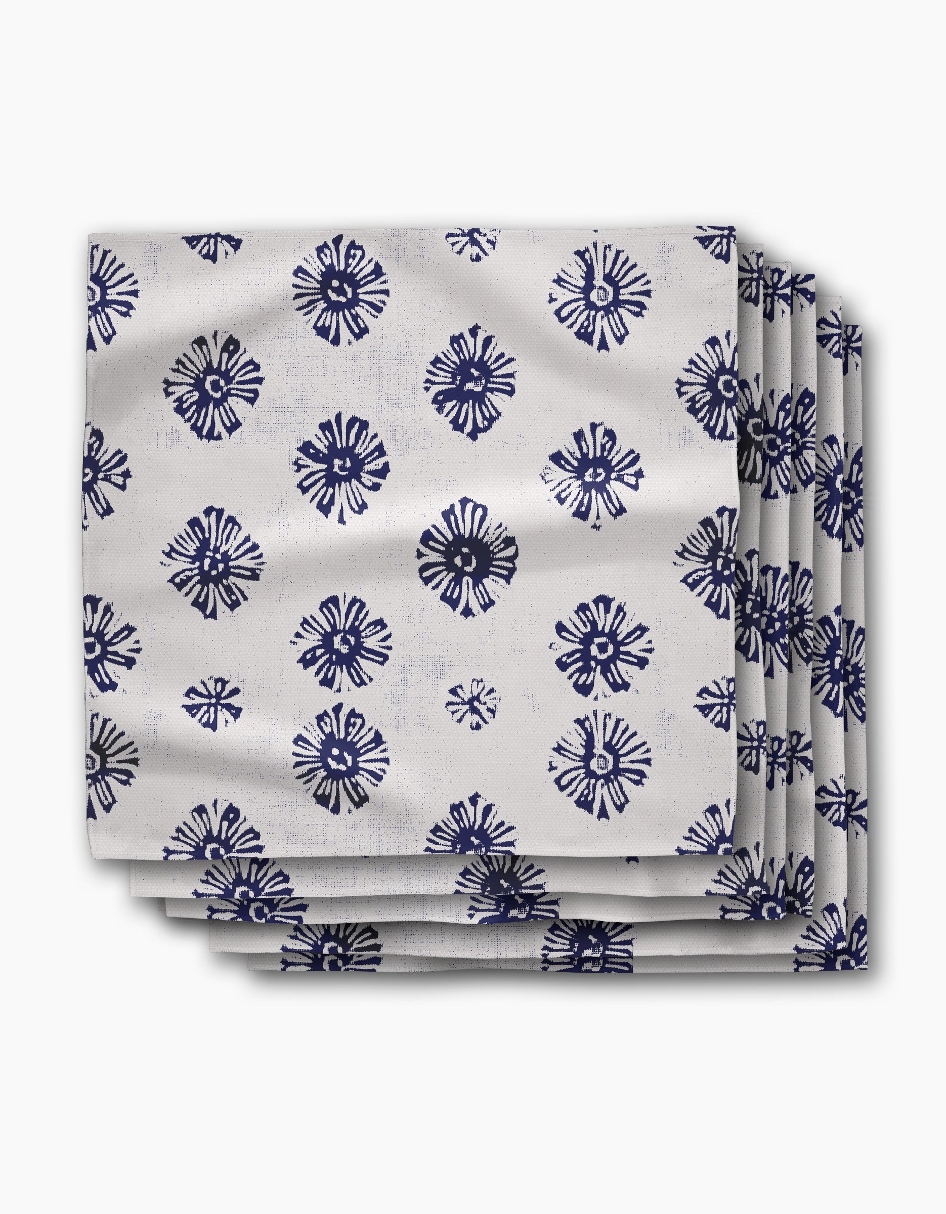 The Leyla White Dinner Napkin Set by Geometry features four white napkins made from recycled Geosuede fabric, adorned with navy circular floral designs. Eco-friendly and elegant, neatly stacked for a refined table setting.