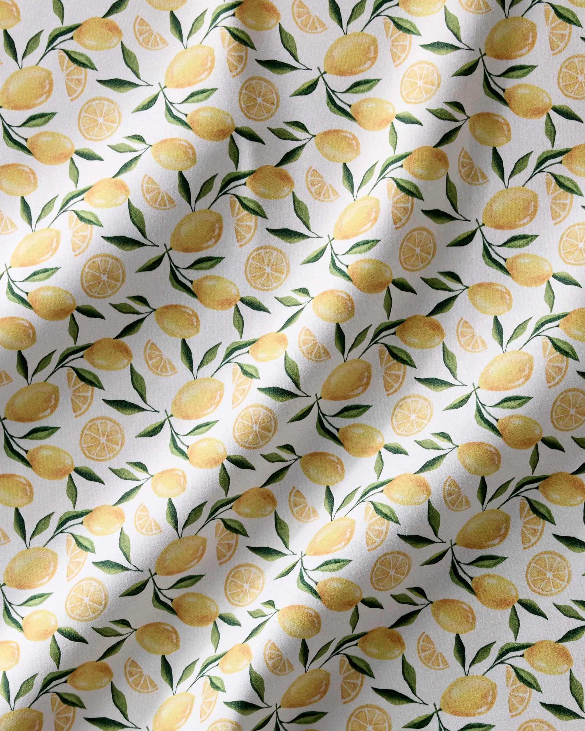 The Limoncello recycled dinner napkins by Geometry feature a seamless pattern of whole lemons, lemon slices, and green leaves on white Geosuede fabric with soft shadows for a wavy texture.