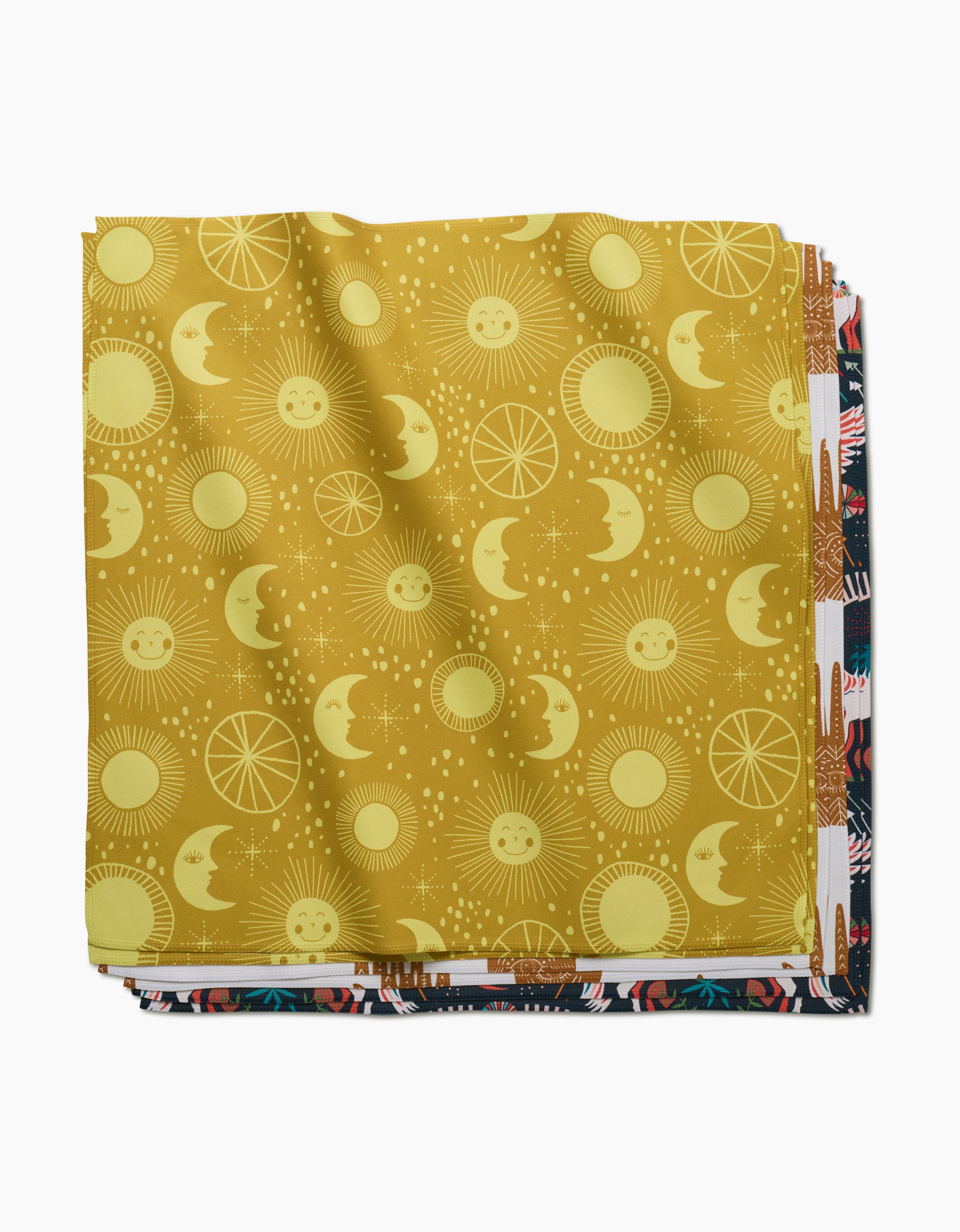 A stack of folded fabric squares, with Jessica Swift’s Magical Moments on top—a yellow print with smiling suns, moons, and stars—makes perfect eco-friendly napkins for your Dinner Napkin Set. Other colorful patterns peek out below.