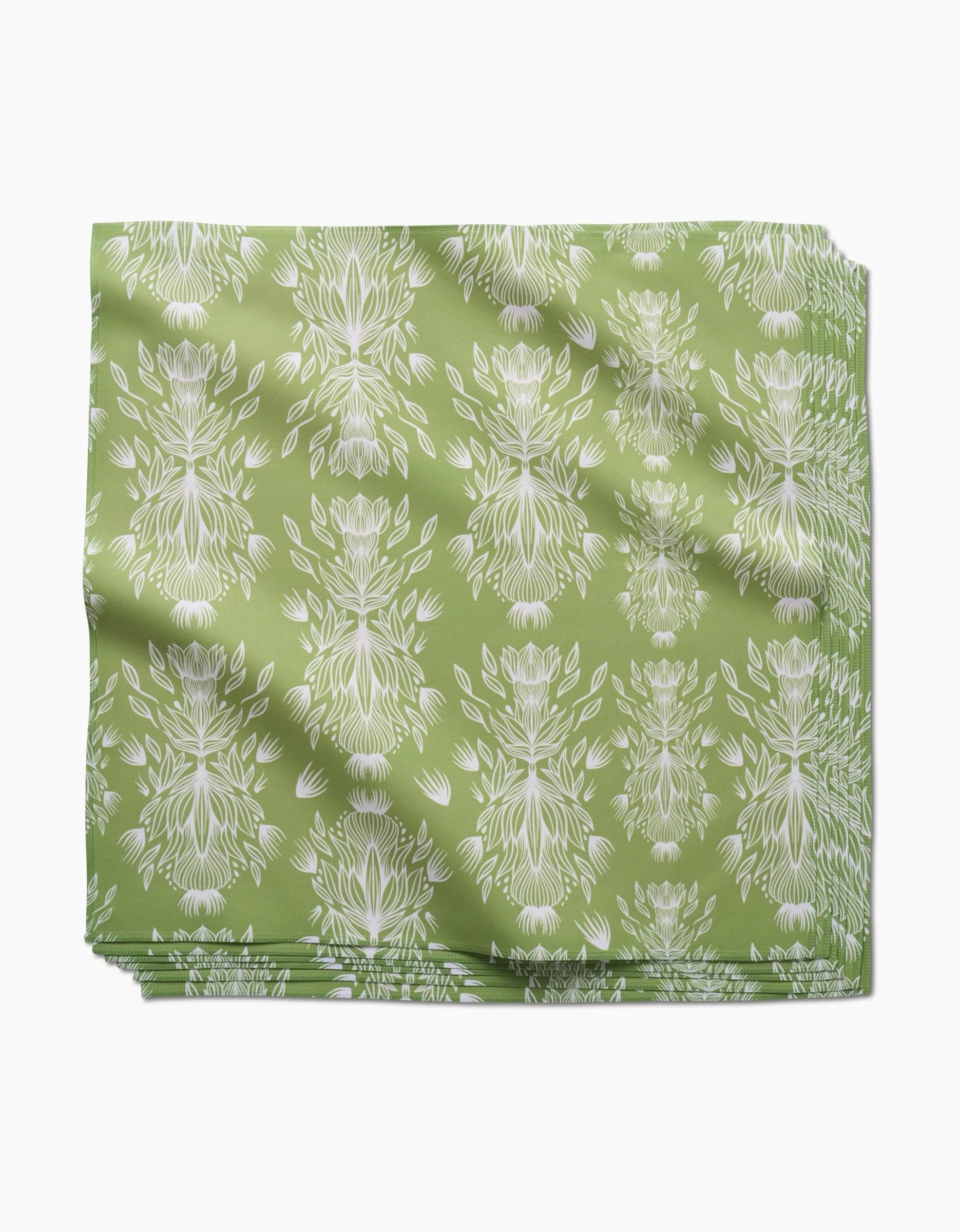 The GEOMETRY Margarita Vibes set features green Geosuede dinner napkins with a white floral and leaf print, neatly folded with faint creases, displayed on a plain white background.