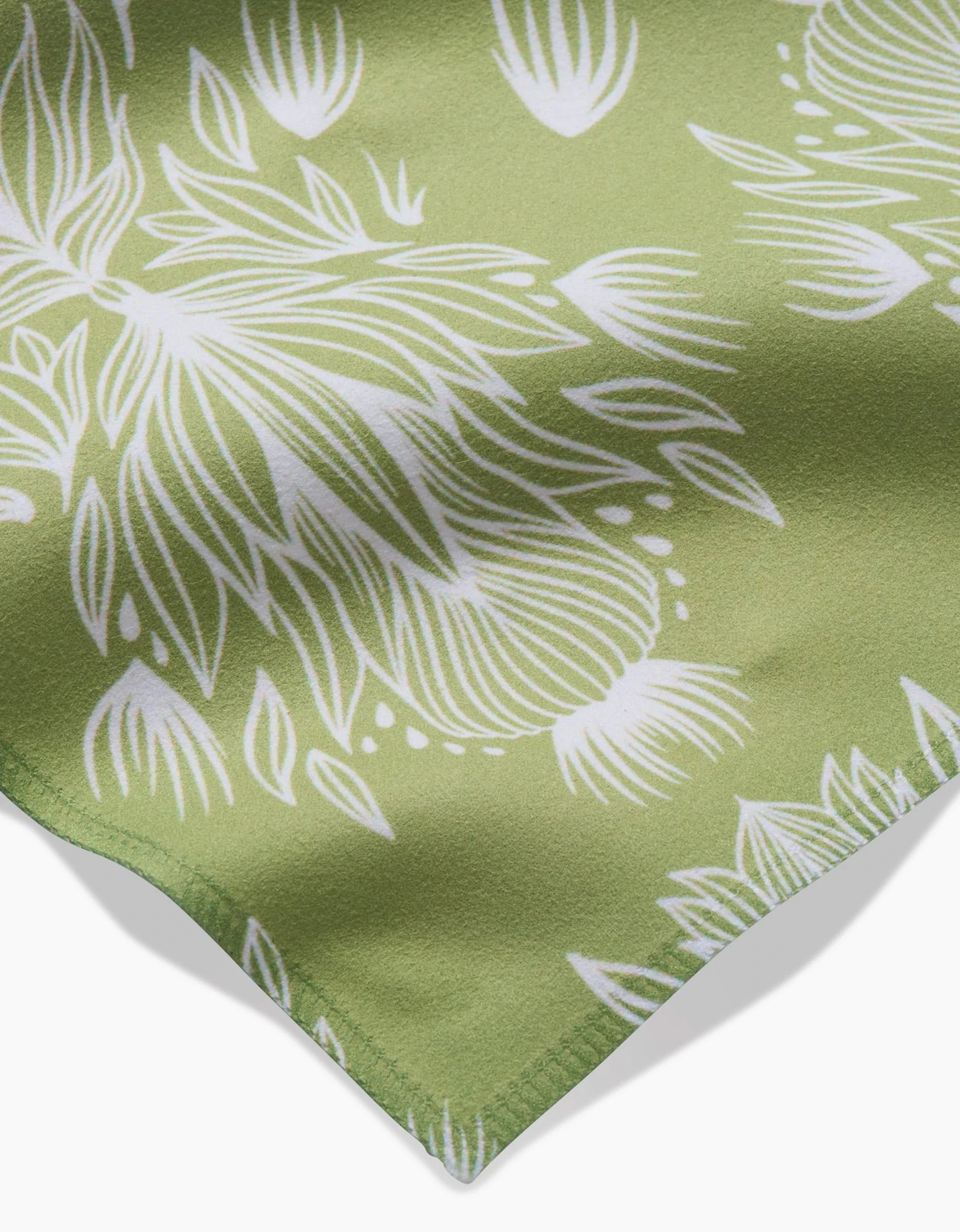A close-up of GEOMETRYs Margarita Vibes, a green Geosuede fabric made from recycled materials with a white abstract floral pattern and neatly stitched edges, draped at an angle.
