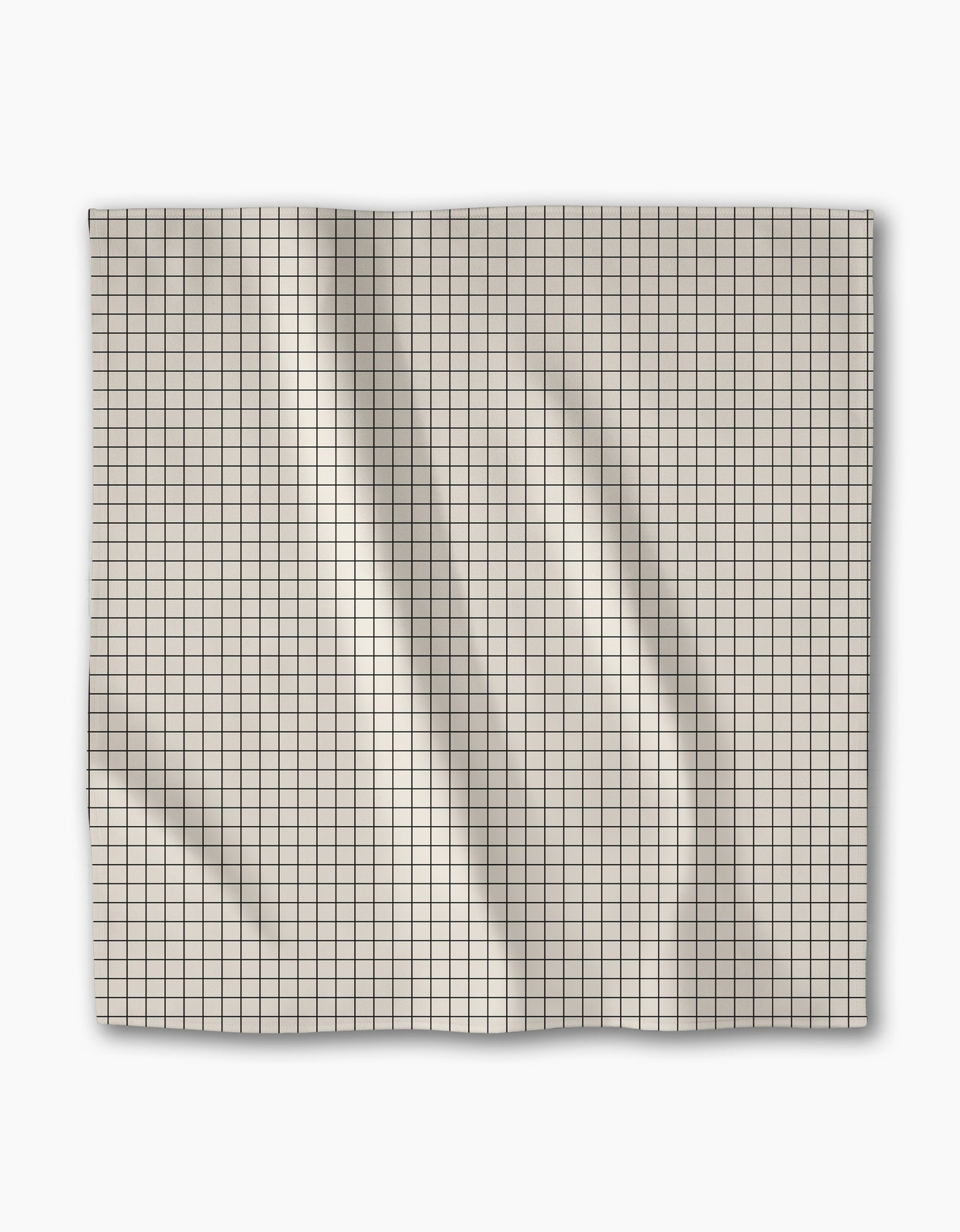 The Geometry Metro Grid dinner napkin features light-colored Geosuede fabric in a square shape with a small black grid pattern, displayed flat on a white background showing creases and folds.