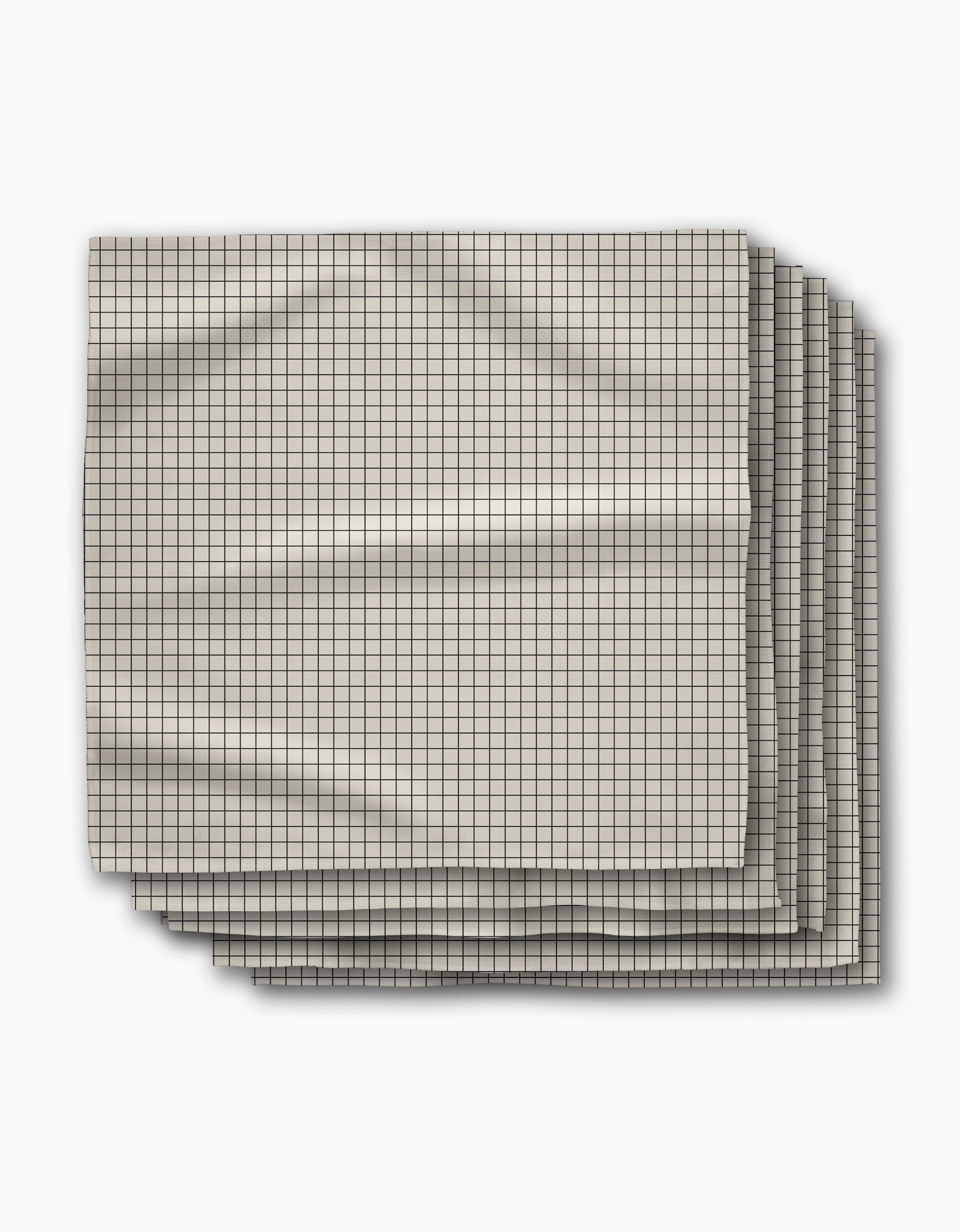 Four folded Metro Grid dinner napkins by Geometry, featuring a small black grid pattern on light beige Geosuede fabric, are stacked slightly offset on a white surface with visible creases.