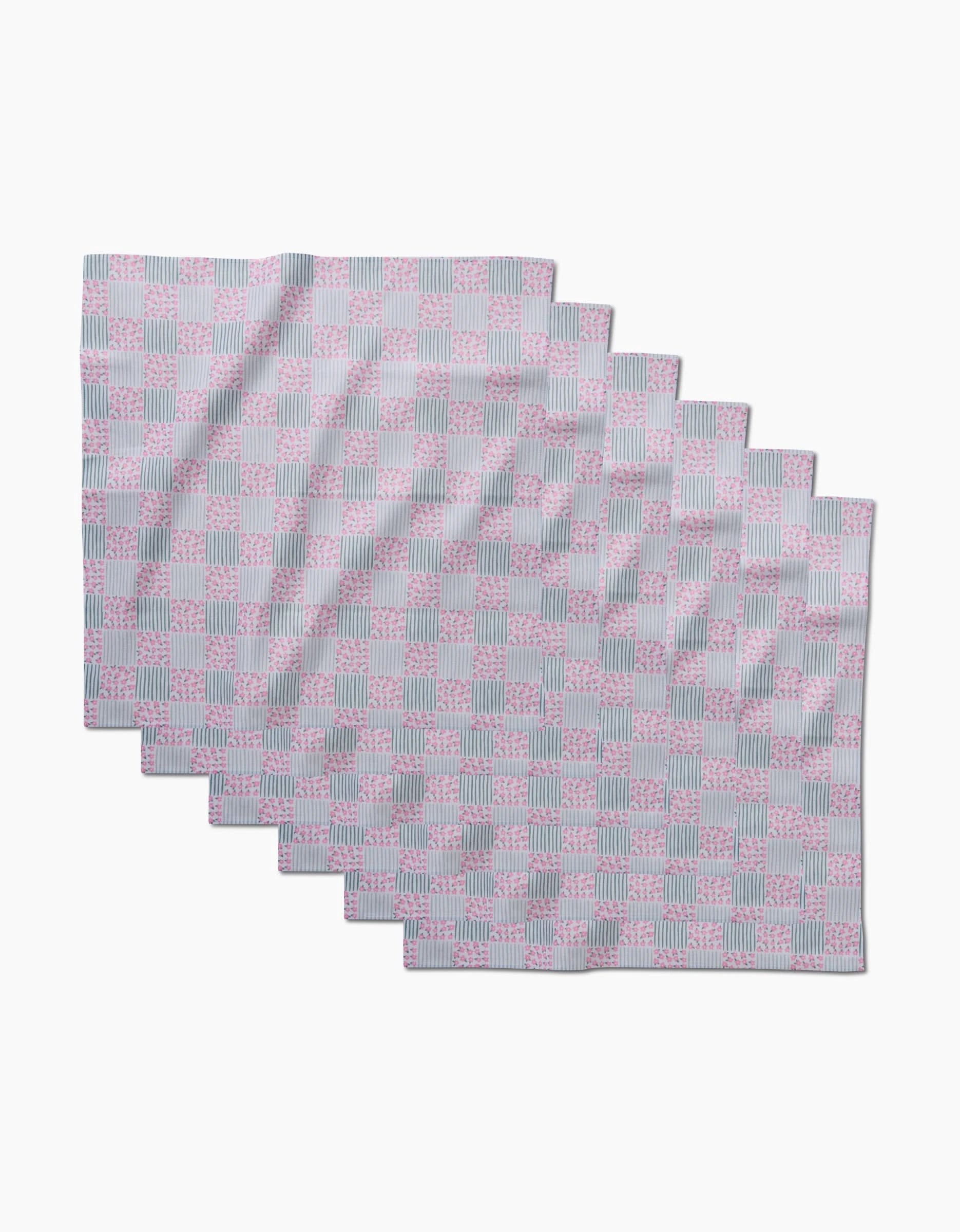 Seven rectangular placemats from Hufton Studio’s Mini Flowers and Stripes Check collection, featuring a pastel pink and blue checkered pattern, are arranged in a staggered, overlapping layout on a white background.