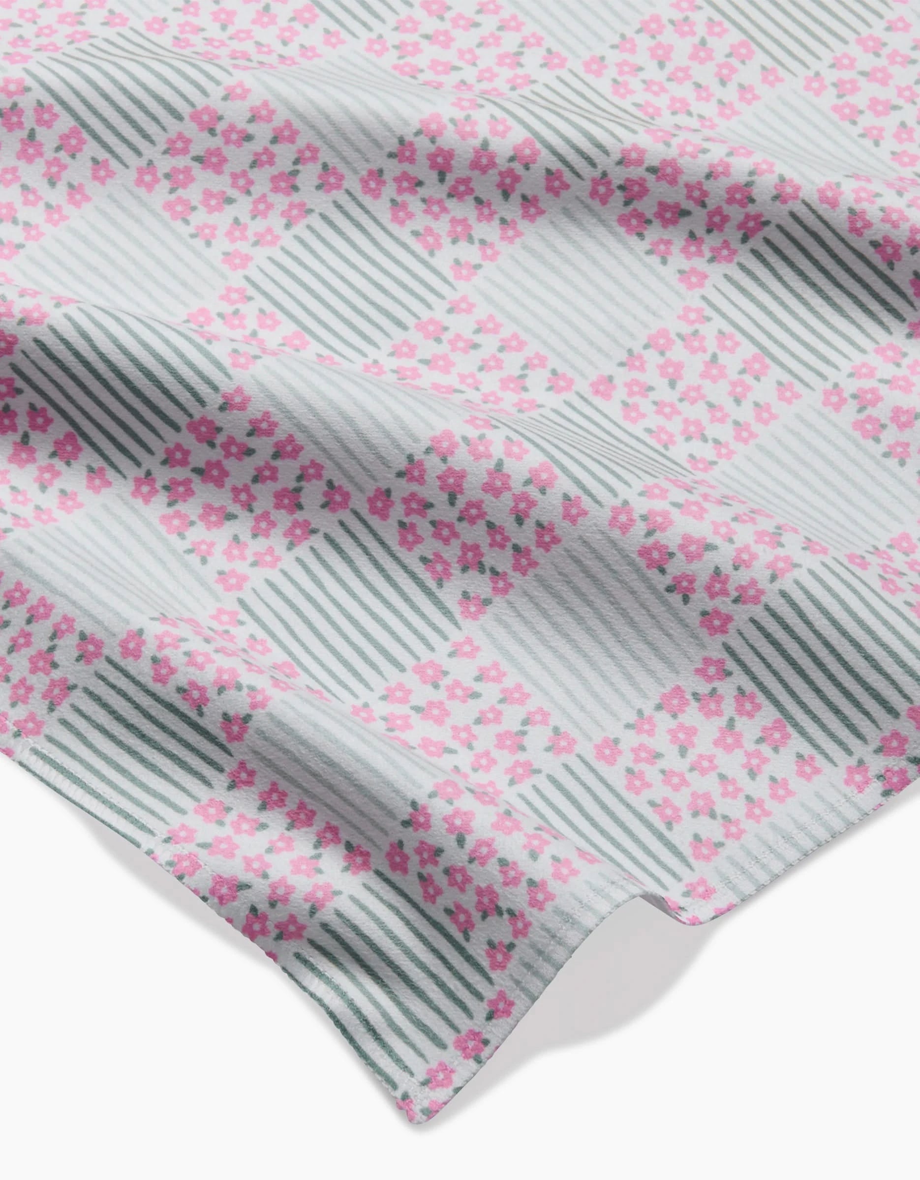 A slightly wrinkled piece of Hufton Studio’s Mini Flowers and Stripes Check Geosuede fabric, made from recycled materials, features a checkered pattern of pink flowers and green stripes on a white background.