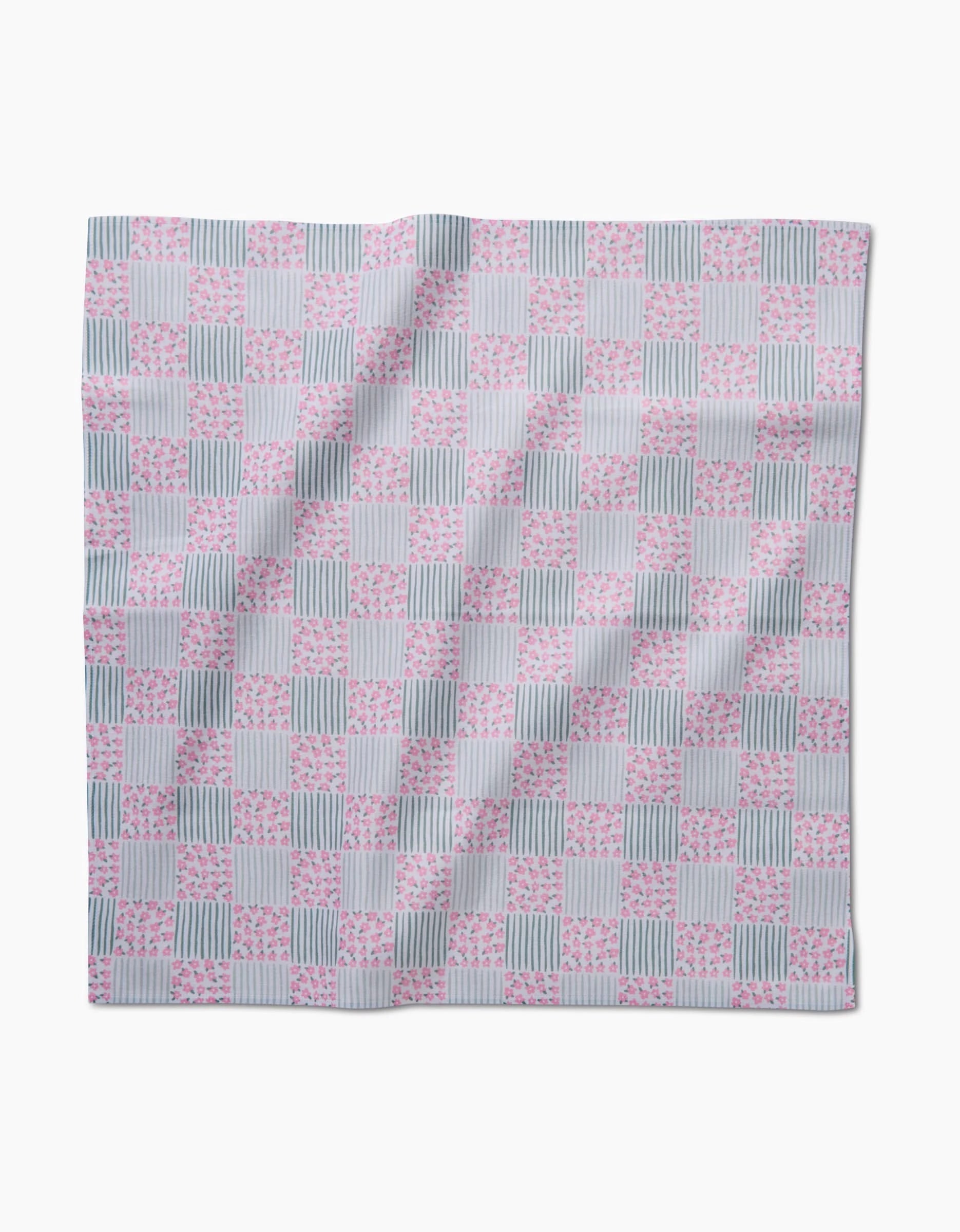 The Mini Flowers and Stripes Check by Hufton Studio is a square dinner napkin with alternating pink floral and green striped squares on a white Geosuede background, shown laid flat with slight wrinkles.