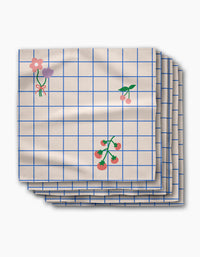 The Mini Harvest dinner napkin set by Letters By Shells features cream-colored Geosuede recycled fabric with a blue grid and charming flower, cherry, and tomato illustrations.