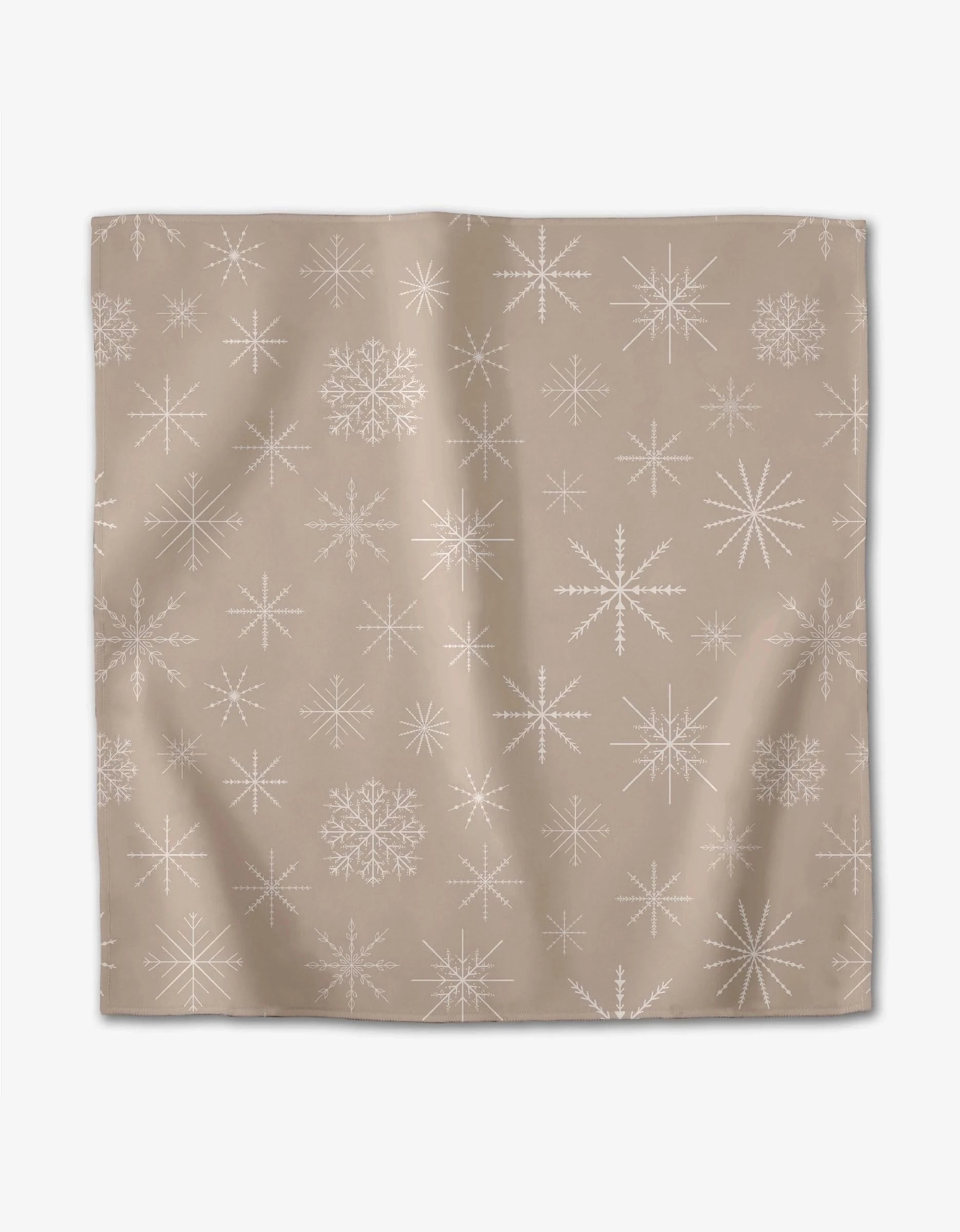 The Minimal Snowflakes dinner napkin by Rosa Kichline is a square beige cloth with white snowflake and starburst patterns, featuring a soft, absorbent texture and subtle folds.