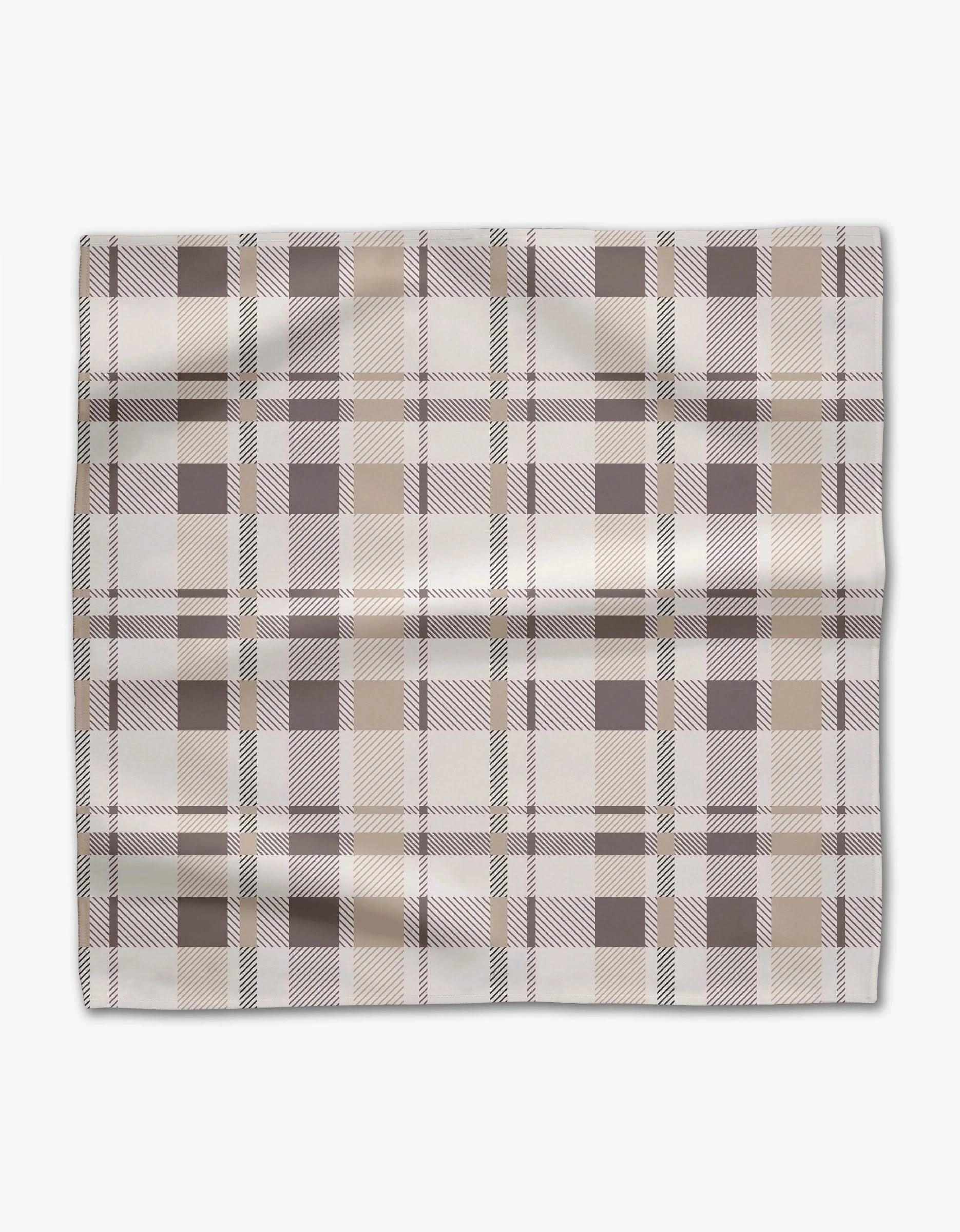 The Minimal Snowflakes dinner napkin by Rosa Kichline is square, absorbent, and features a plaid pattern in beige, brown, and off-white. It’s shown laid flat on a white background with slight fabric folds and creases.