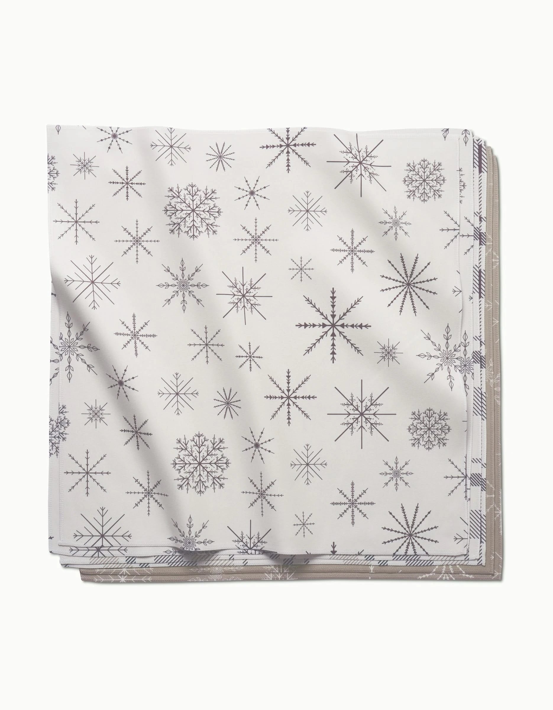 A stack of absorbent Minimal Snowflakes dinner napkins by Rosa Kichline, featuring gray snowflake patterns in various sizes and styles on a white background.