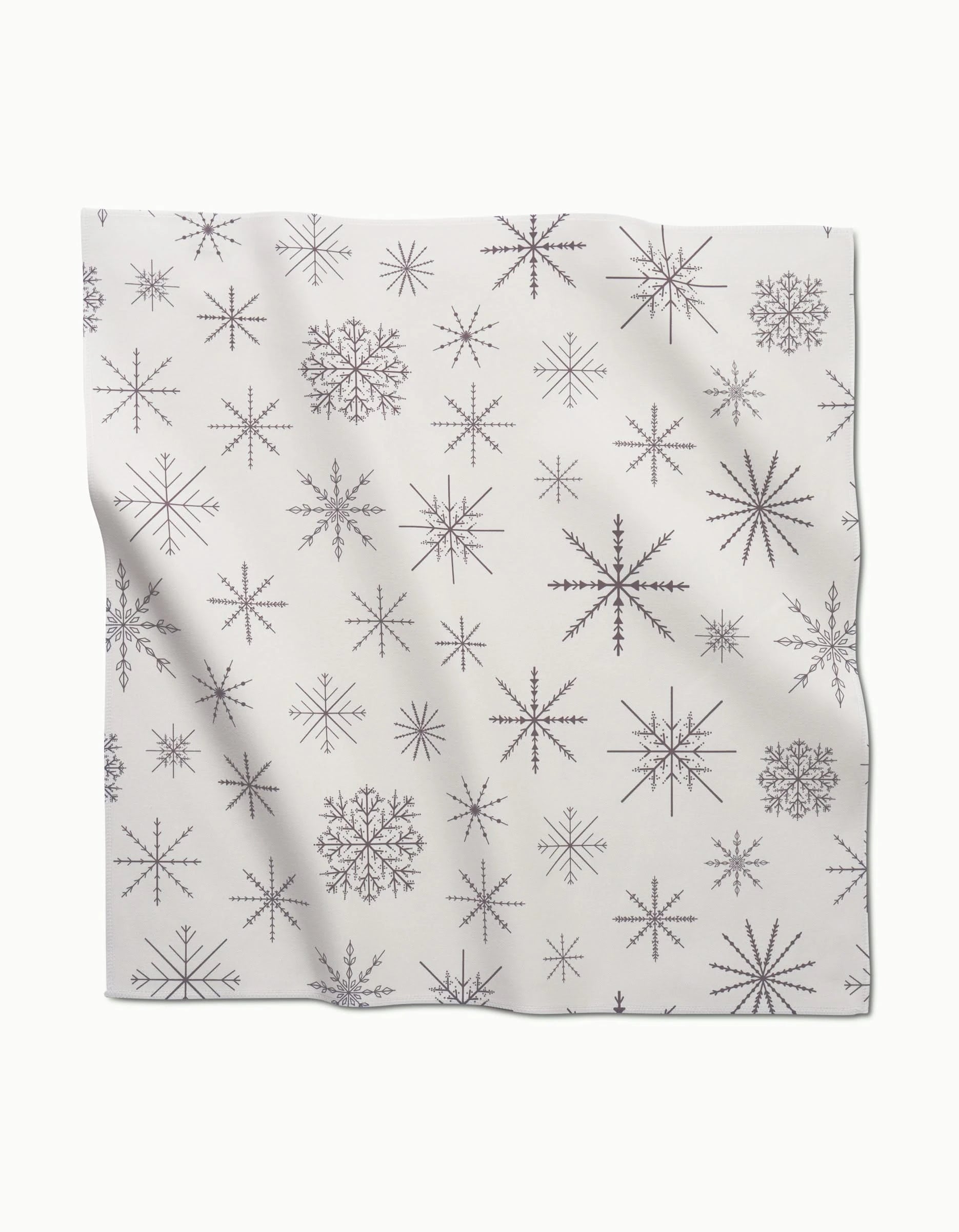 The Rosa Kichline Minimal Snowflakes set features elegant white dinner napkins with absorbent fabric and a repeating pattern of intricate black snowflakes.