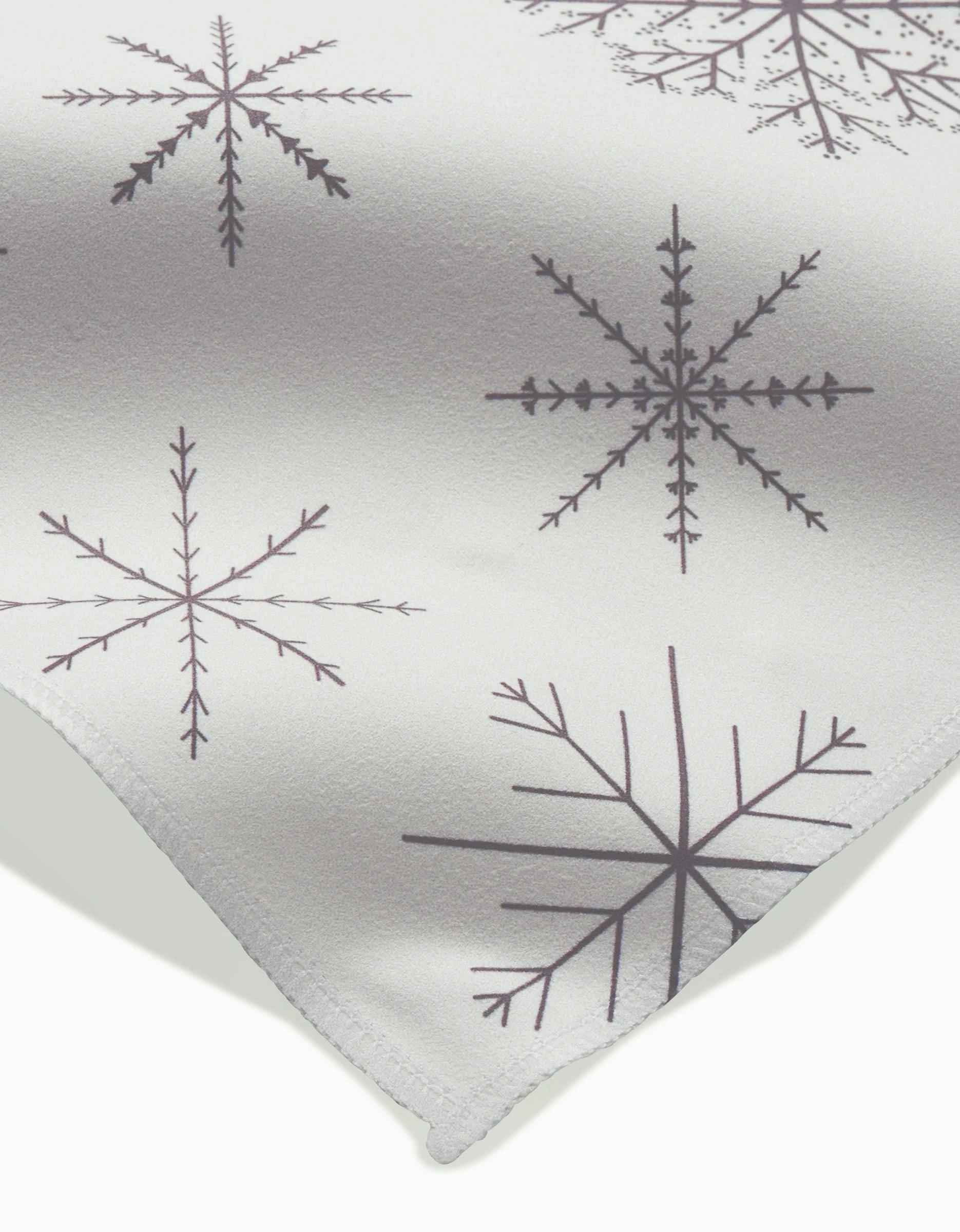 A close-up of Rosa Kichlines Minimal Snowflakes Dinner Napkin Set shows white napkins with dark gray symmetrical snowflake patterns and visible edge stitching, crafted from absorbent fabric.