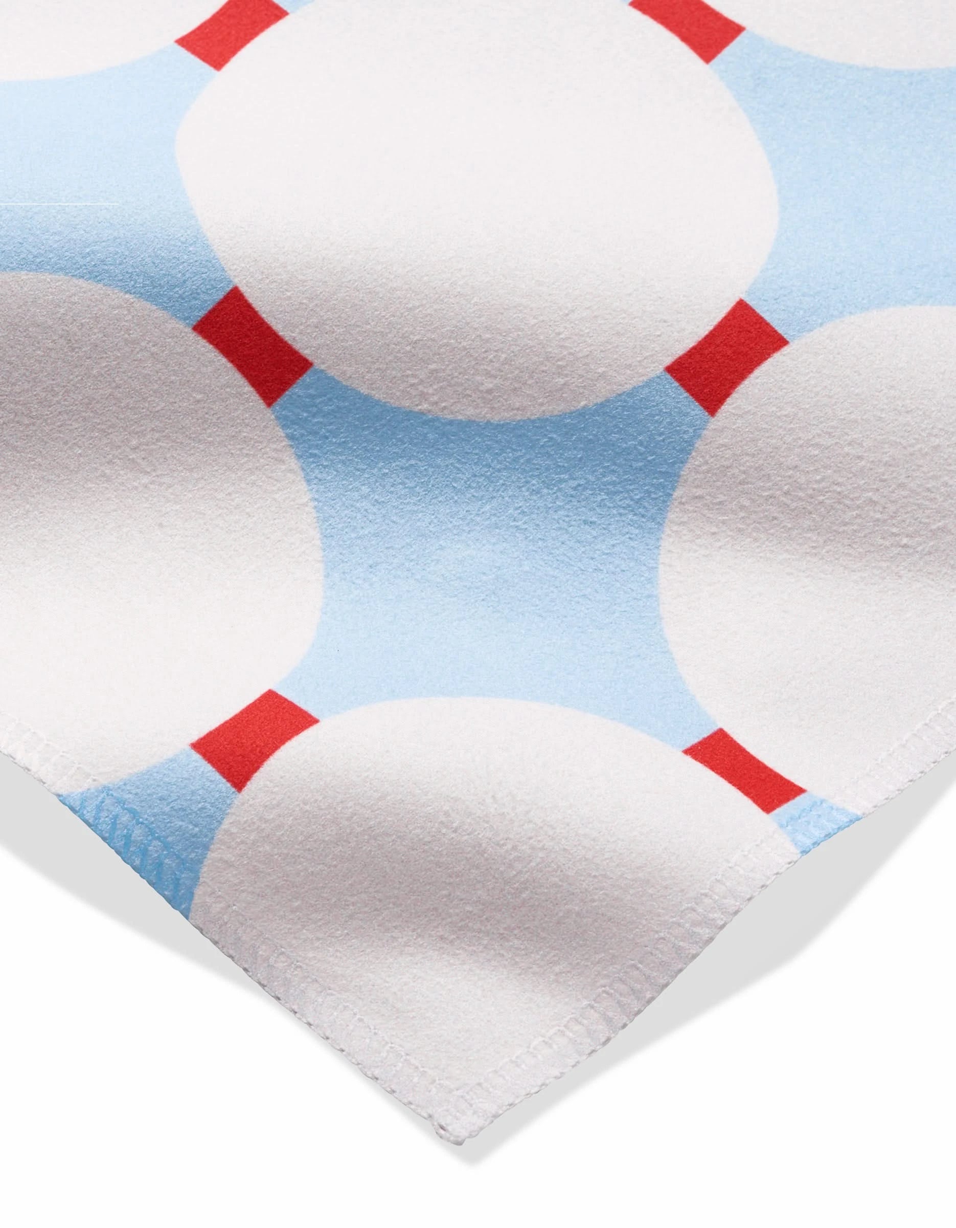 A close-up of Mist Blue Oasis by Happy Hemera shows soft Geosuede fabric with large white circles connected by small red rectangles on a light blue background and a neatly stitched corner.