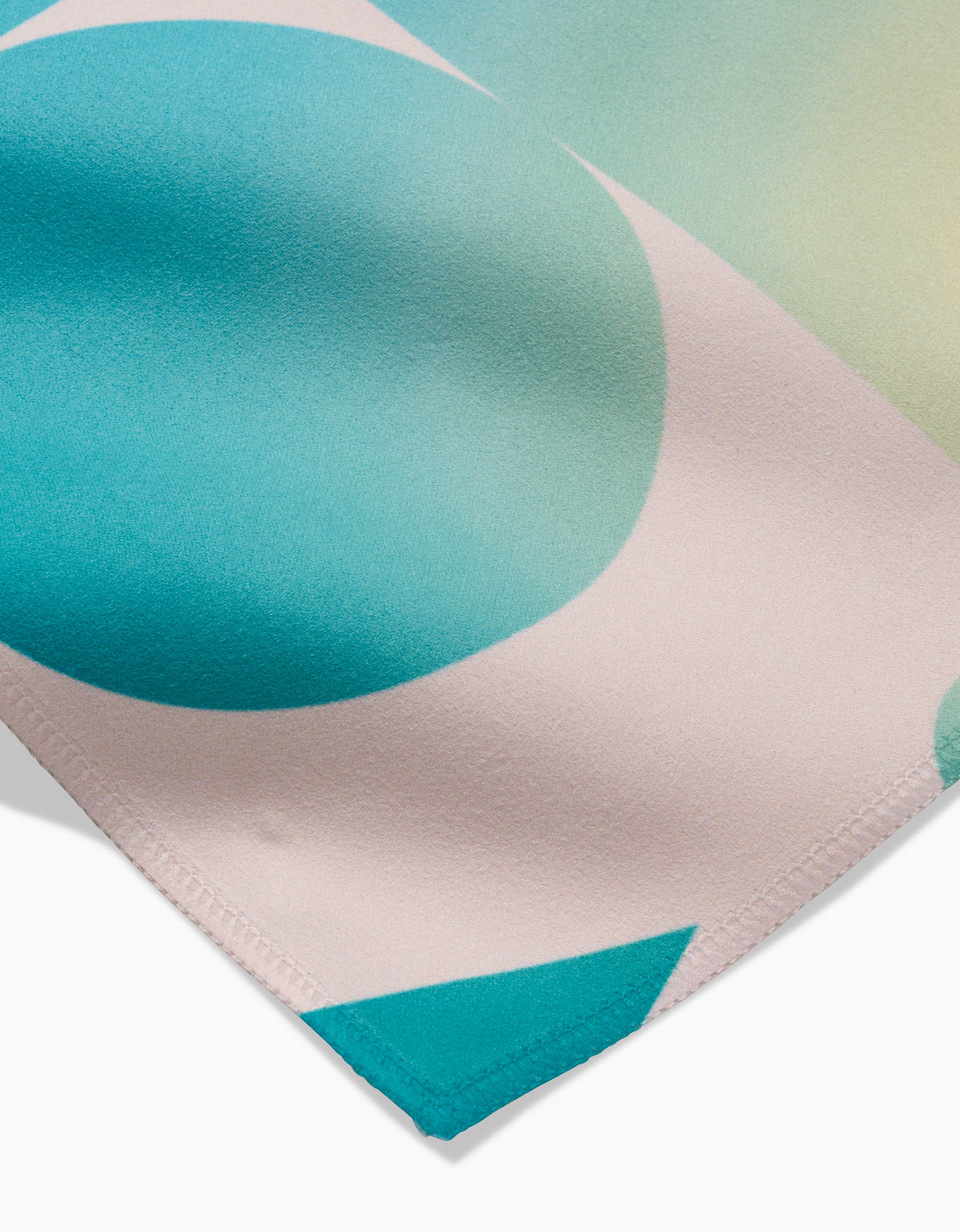 Close-up of GEOMETRYs Moody Shapes Geosuede fabric, showing its smooth texture and modern abstract design in teal, light pink, and soft yellow-green. Stitched edge at bottom right. Made from recycled materials.