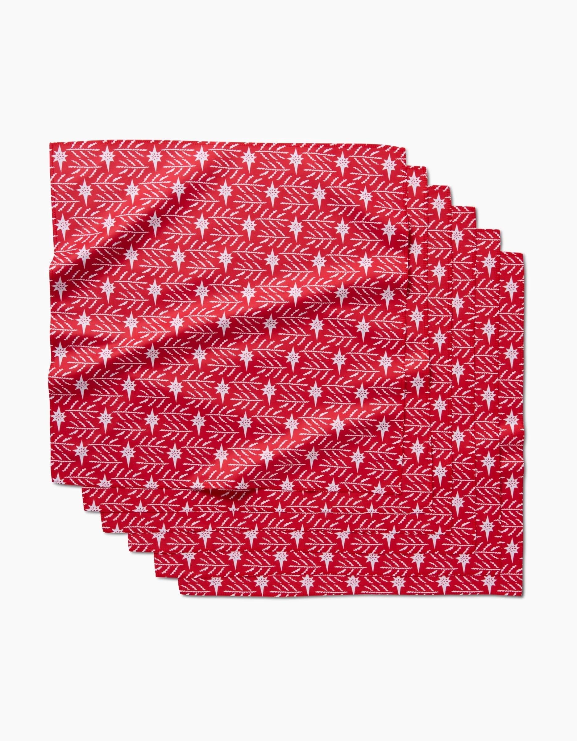 Five red North Star napkins by Roxy Marj, made from recycled materials, feature white holiday-themed trees, stars, and snowflakes. They are neatly stacked and slightly overlapping on a white background.