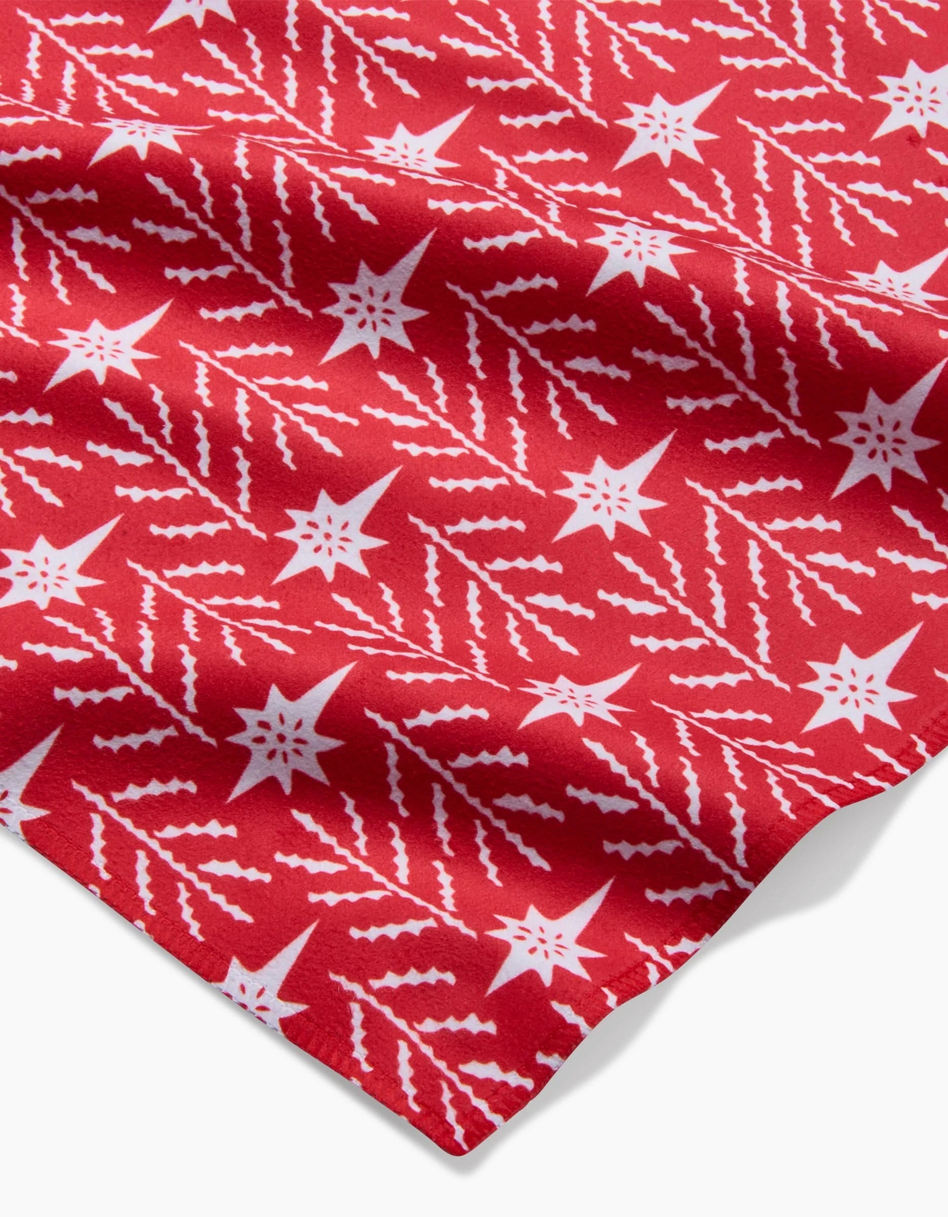 The North Star dinner napkin by Roxy Marj features red Geosuede fabric with white stars and zigzag patterns, slightly wrinkled, viewed from an angle.