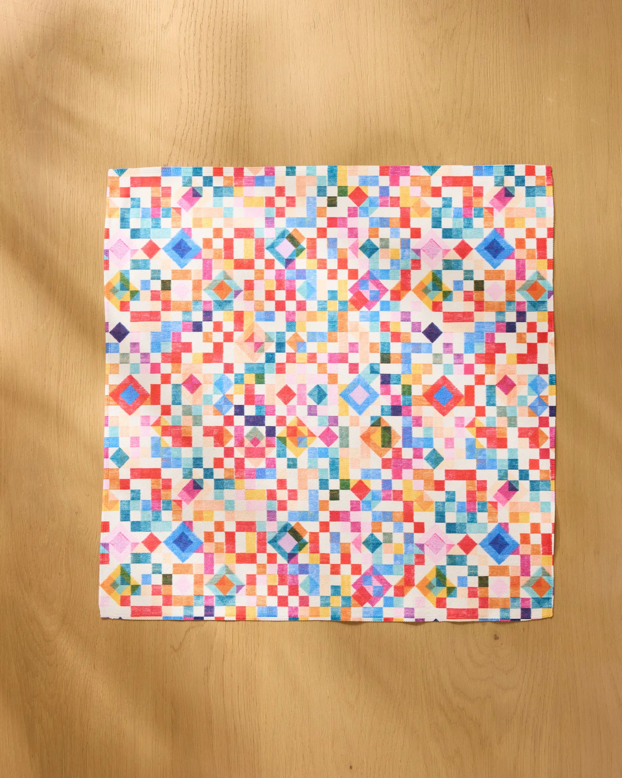 Rachel Parker’s Patchwork Geo—a square quilt with a colorful geometric pattern of small squares and diamonds, shown on light wood—offers bold inspiration for reusable or dinner napkin sets.